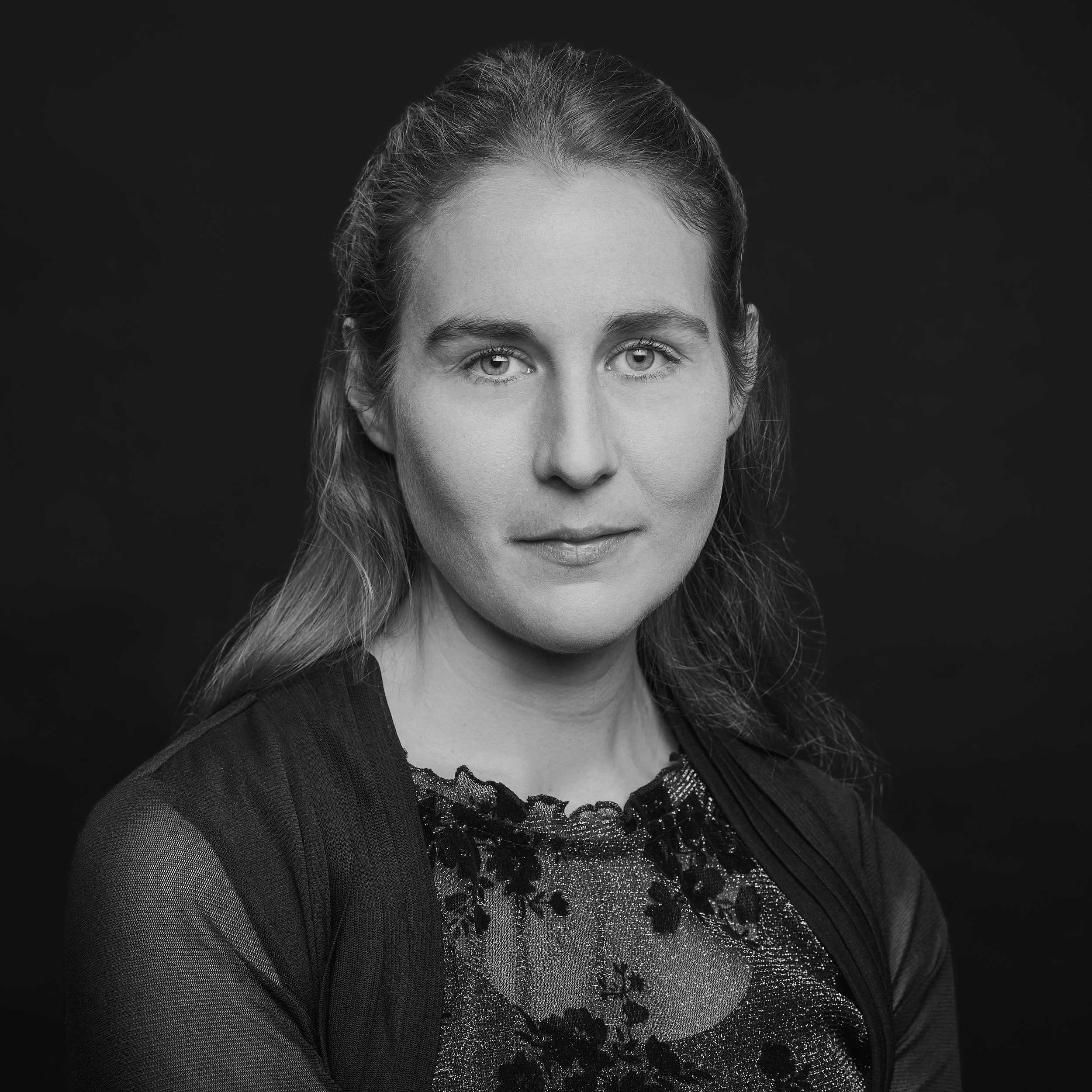 Portrait en noir et blanc d'une femme portant une robe ornée de paillettes et de motifs floraux, avec un fond noir.