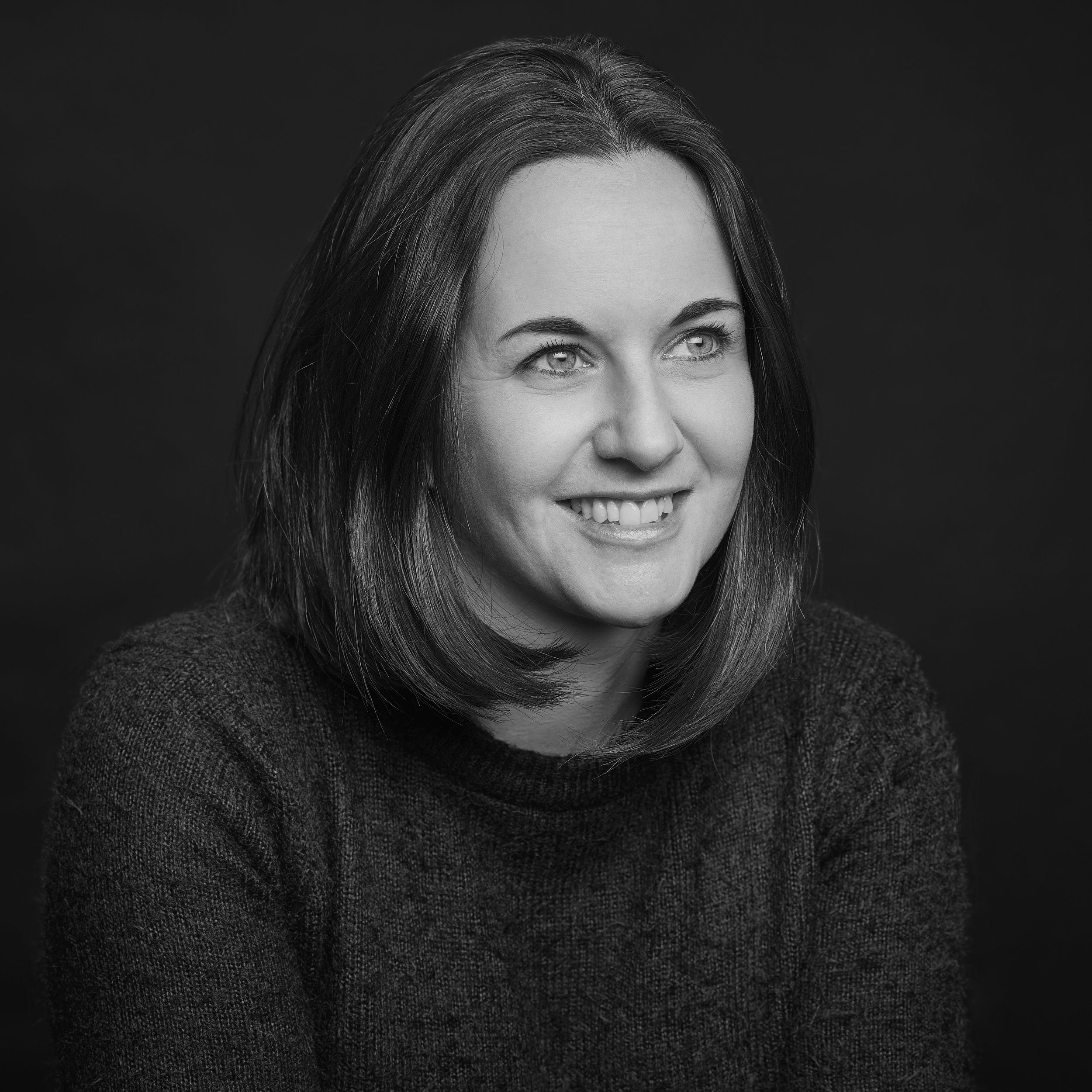 Portrait d'une femme souriante avec des cheveux mi-longs, en noir et blanc, contre un fond sombre.