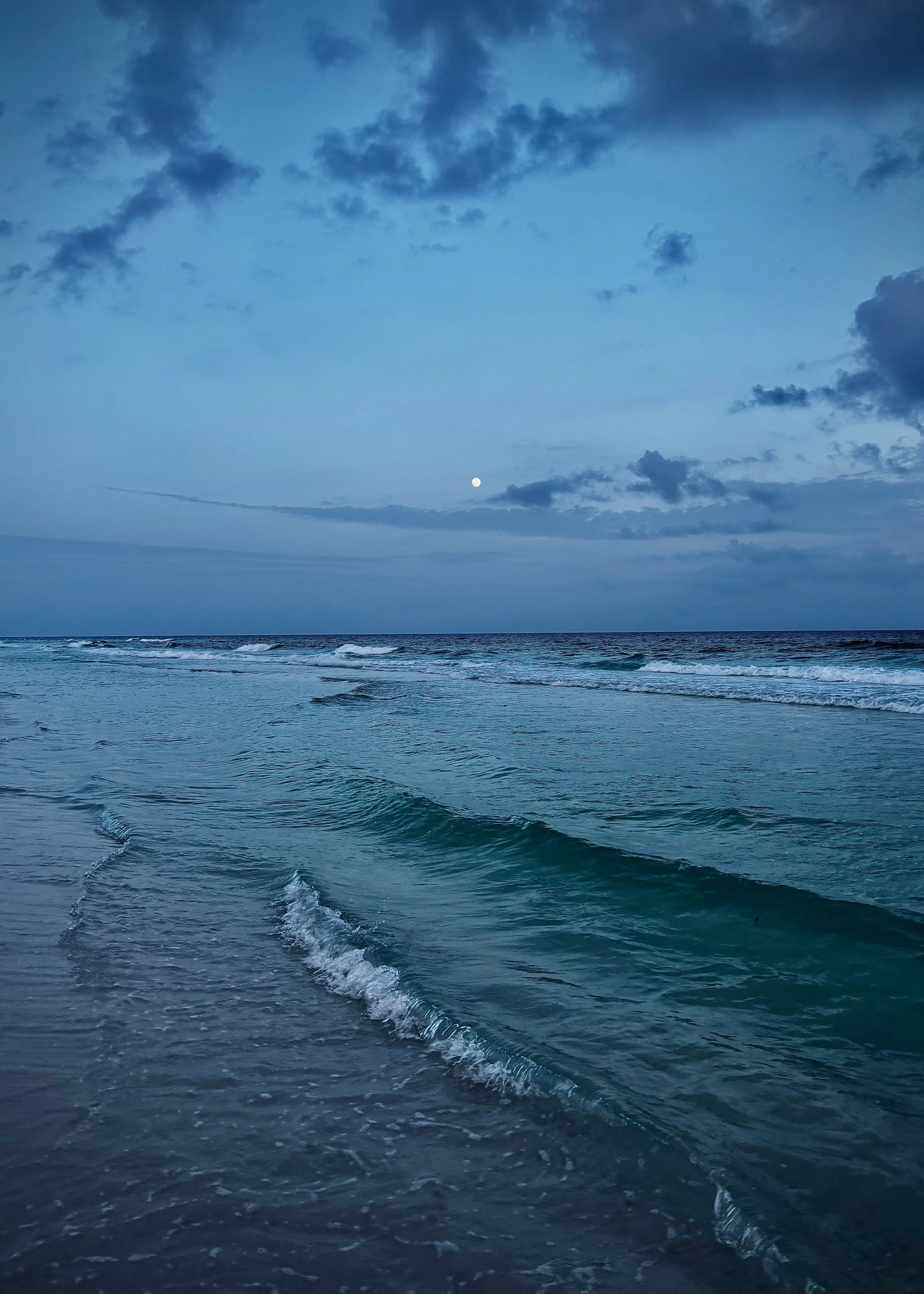 The image shows a serene view of the ocean under a cloudy sky with a visible moon.