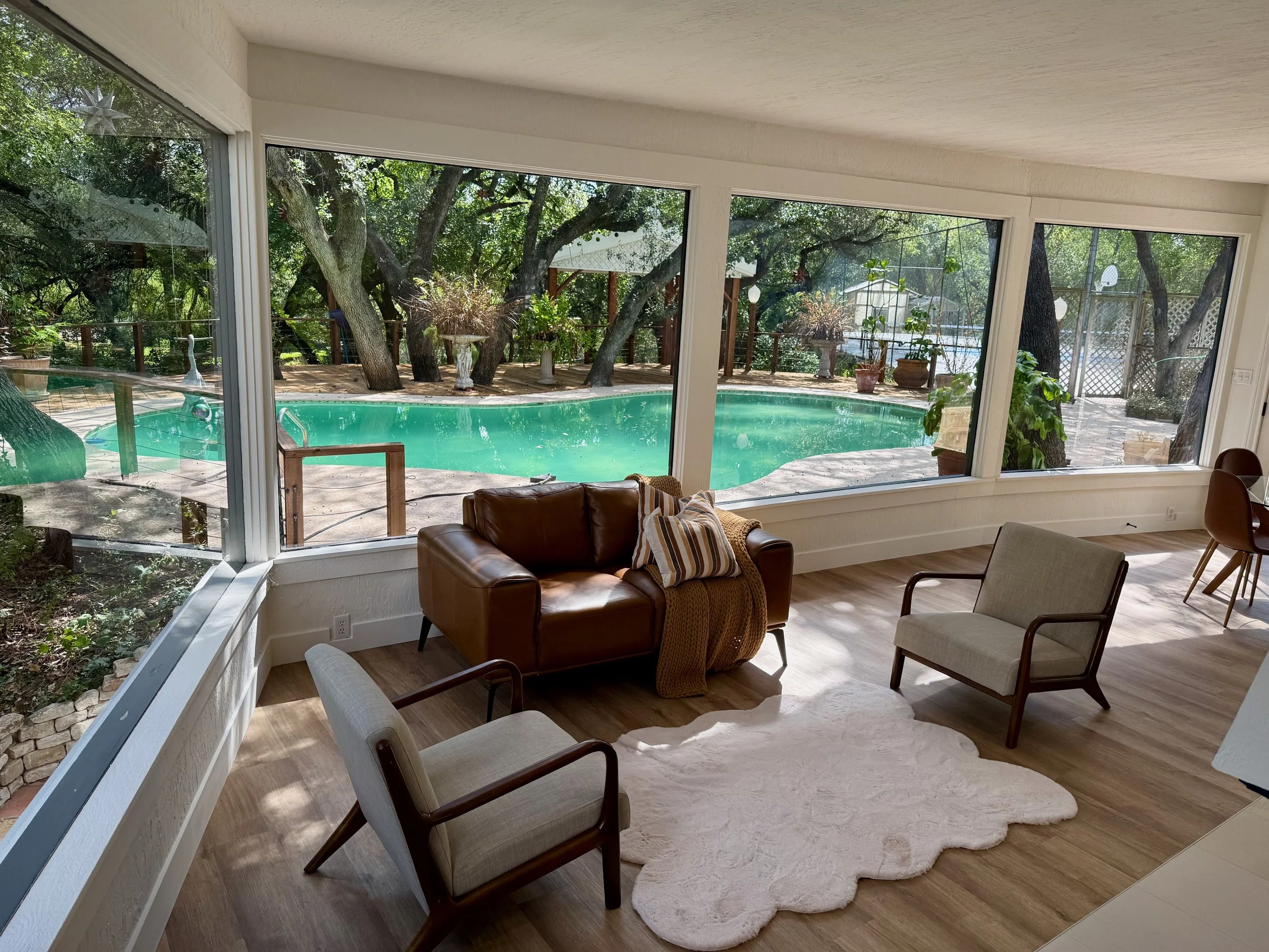 Living room with leather chairs and big windows overlooking a backyard pool