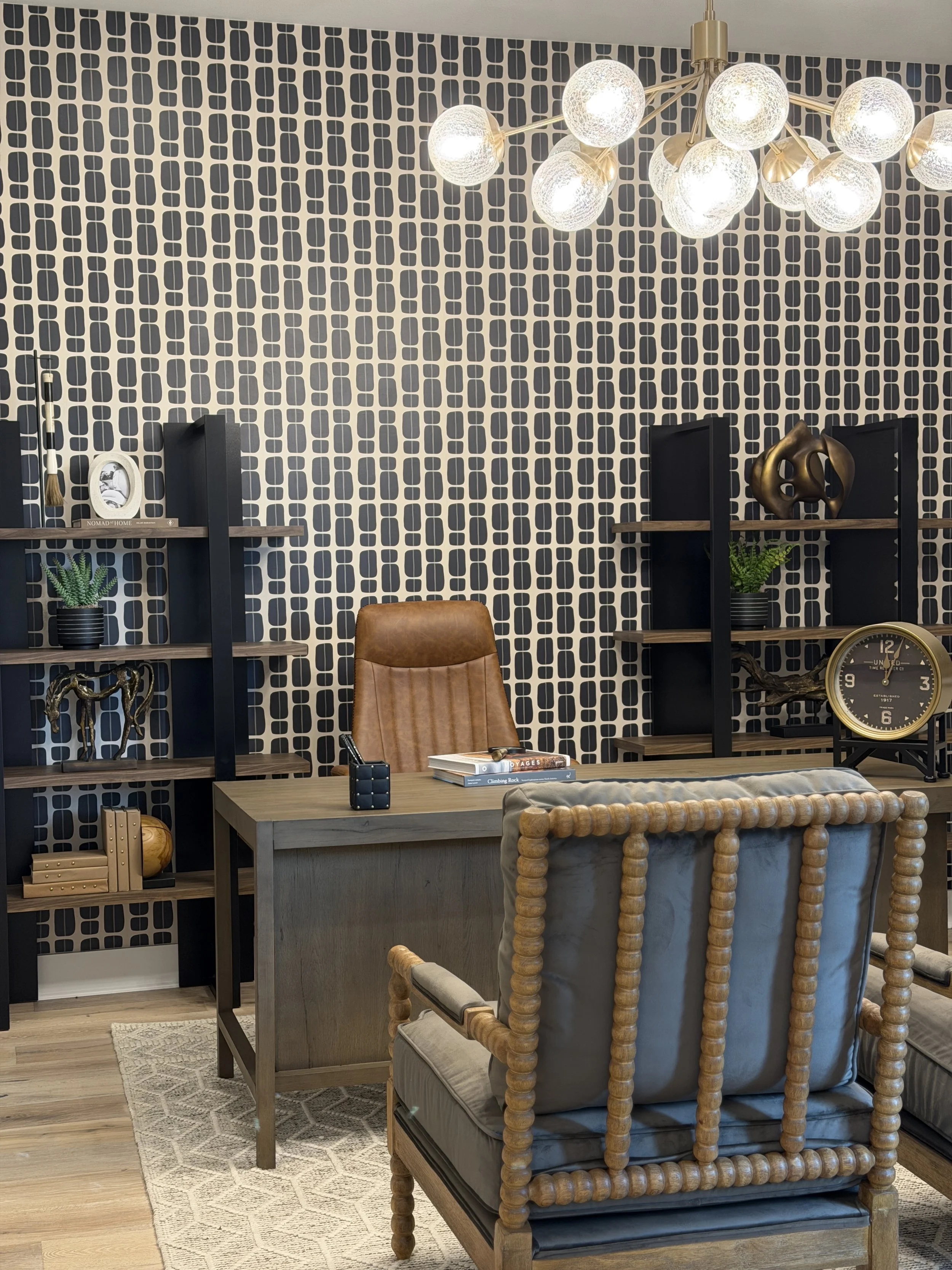 Home office with a patterned accent wall and a globe chandelier