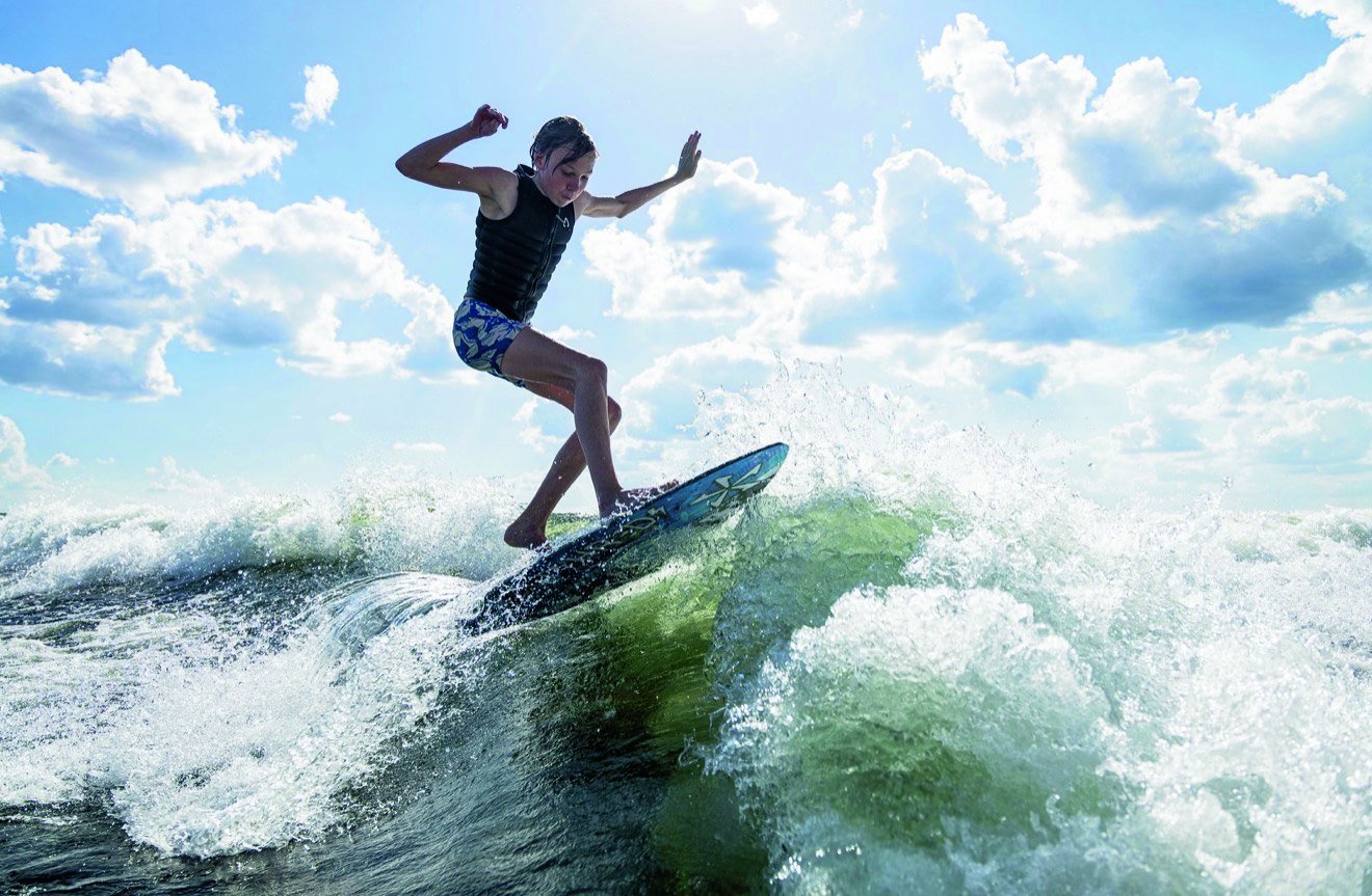Windermere skim rider Declyn Van Der Riet carves across a boat wake on a sunny day