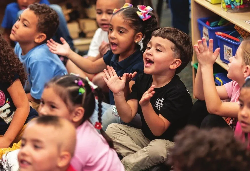 A group of excited young children sitting on the floor, clapping and reacting during a library program
