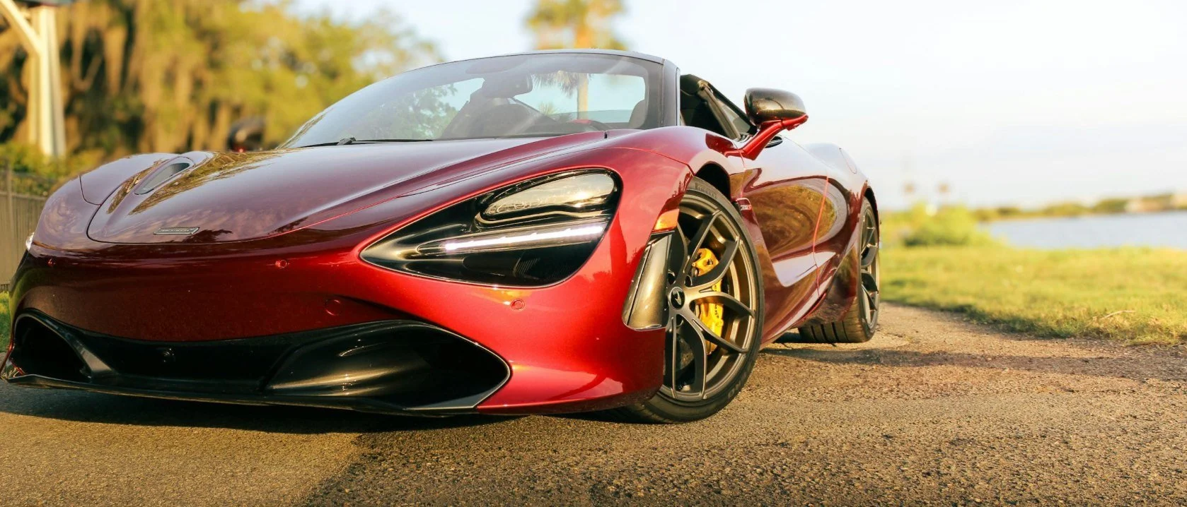 Orange McLaren supercar parked on a lakeside drive at sunset, the kind of car collectors store at Motor Volta