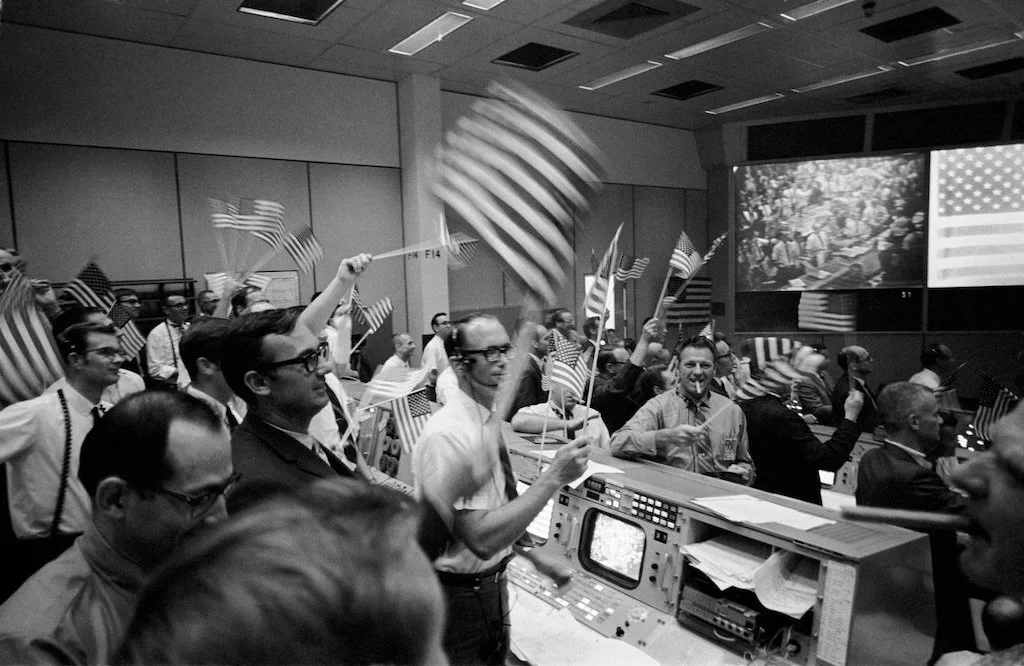 NASA team, holding American flags, celebrating in a control room - a historical scene.