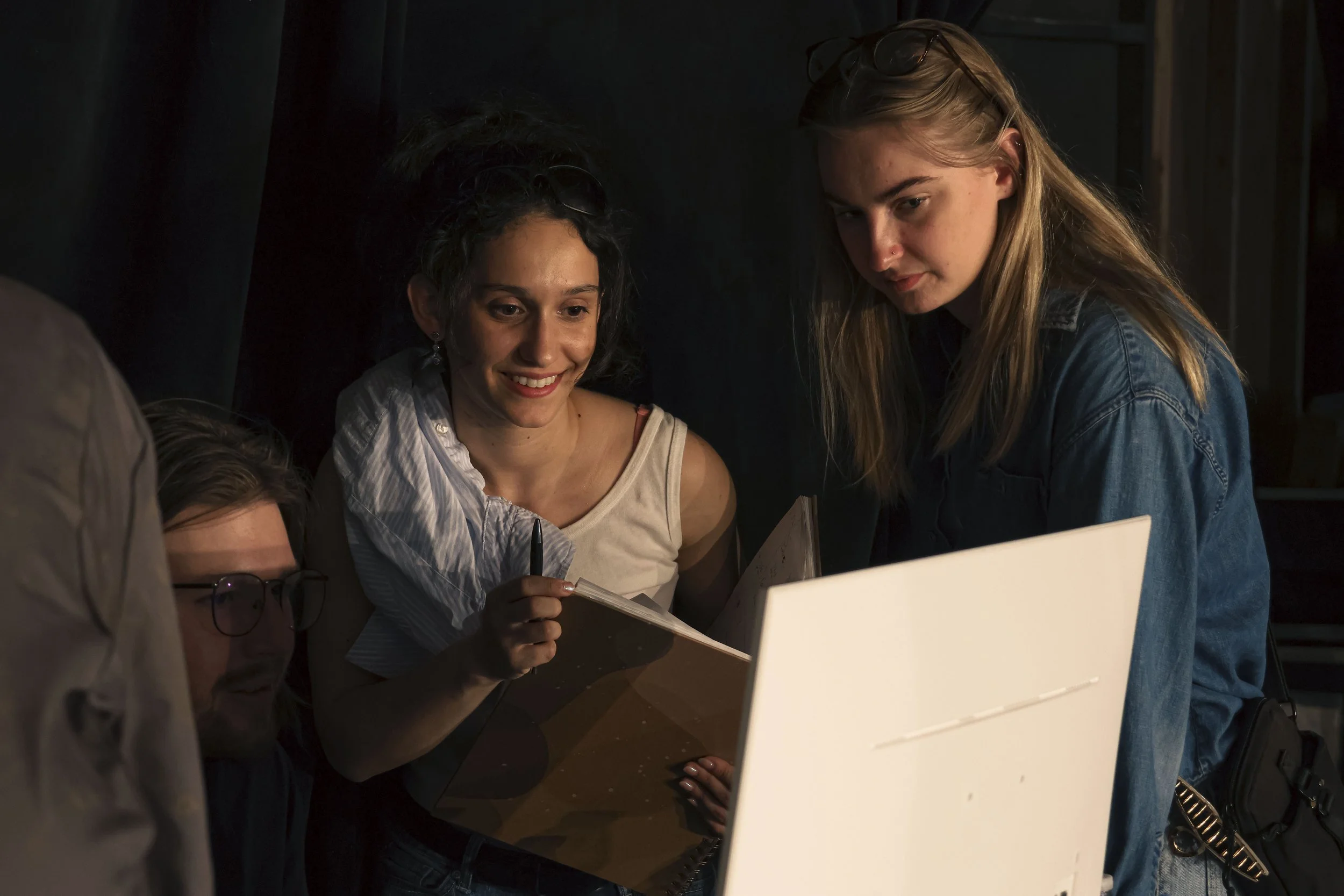 Four women gathered around a table, engaged in a discussion or sharing ideas, with one woman holding a notebook and pen.