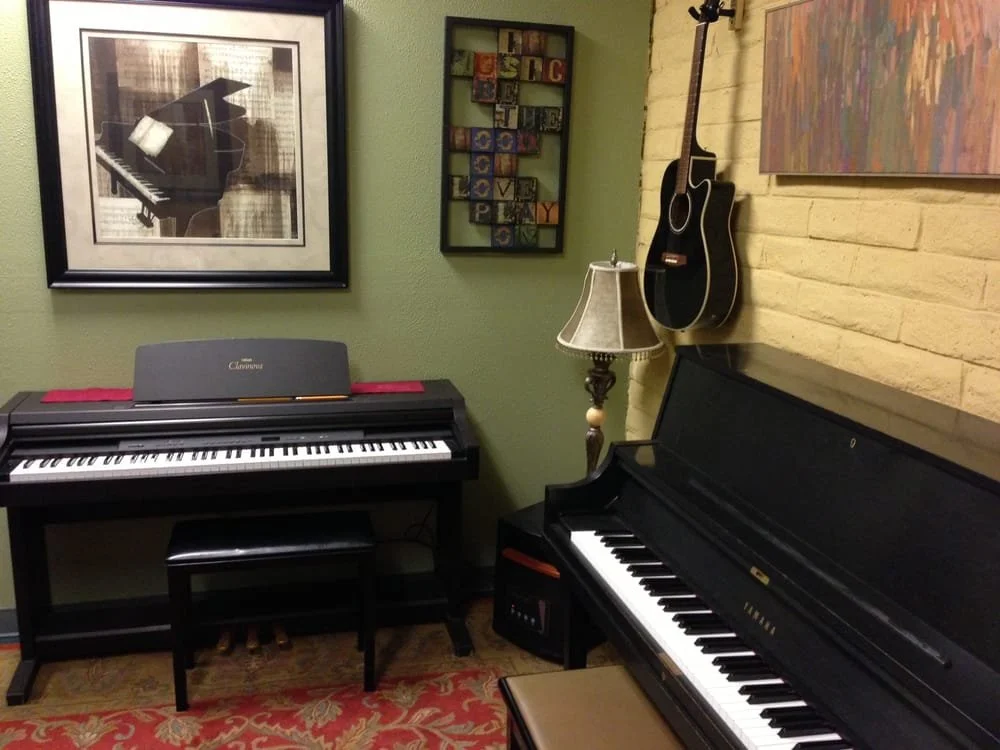 Home music room with a digital piano, upright grand piano, guitar, floor lamp, and musical wall art