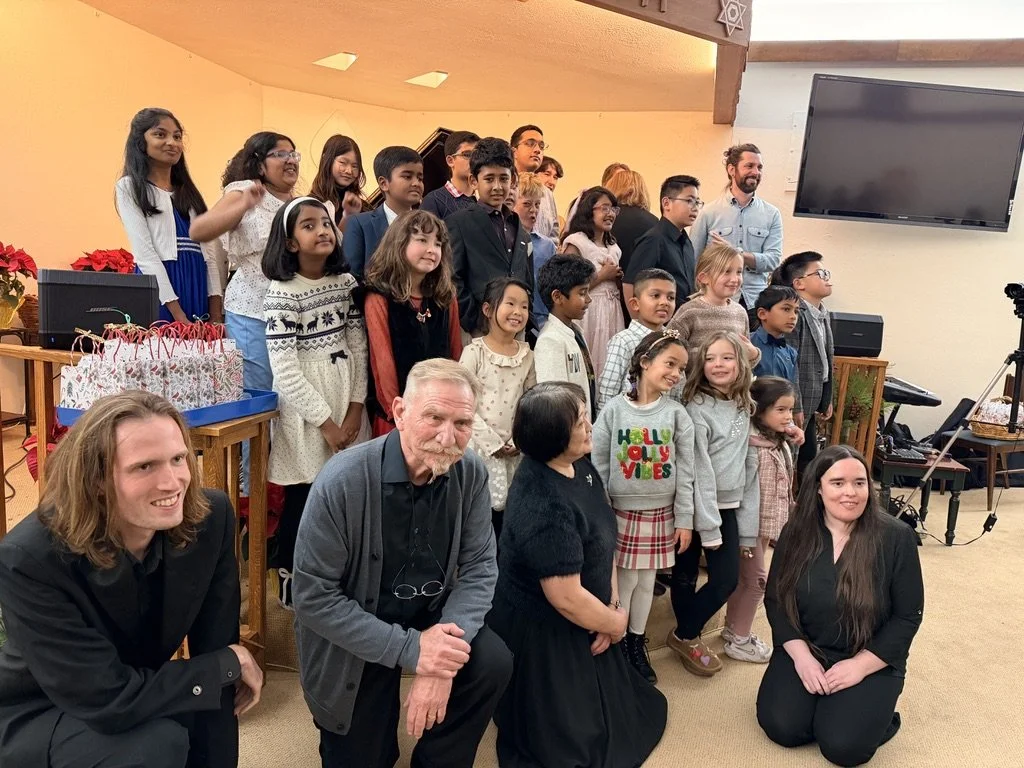 Group of children and adults posing indoors at a holiday celebration with gift bags and decorations
