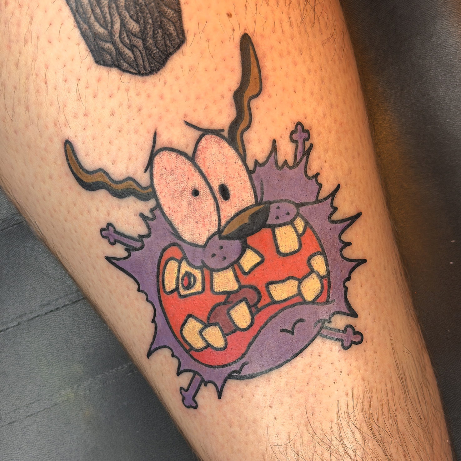 Colorful cartoon Courage The Cowardly Dog tattoo on a person’s leg, work by Ruben.