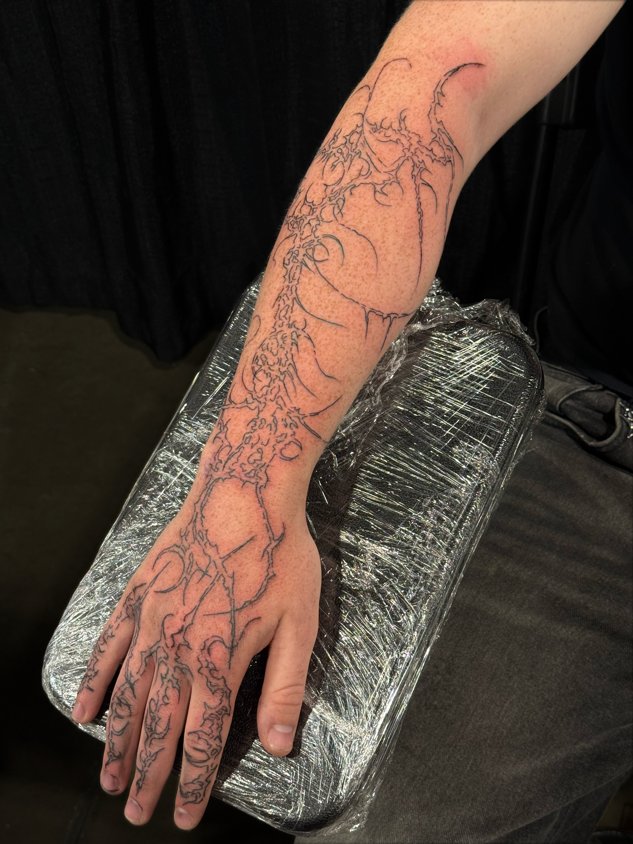 Close-up of a hand and forearm with an intricate dragon tattoo stencil resting on a plastic-wrapped tattoo armrest, work by Hannah.