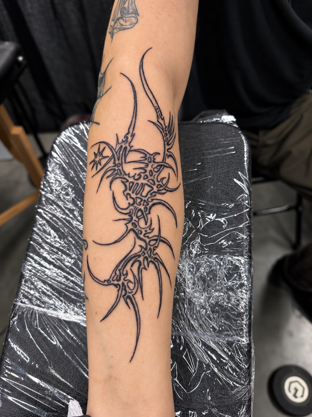 Close-up of an arm with an intricate black-line tattoo featuring abstract cyber designs in a tattoo studio. Work by Hannah.