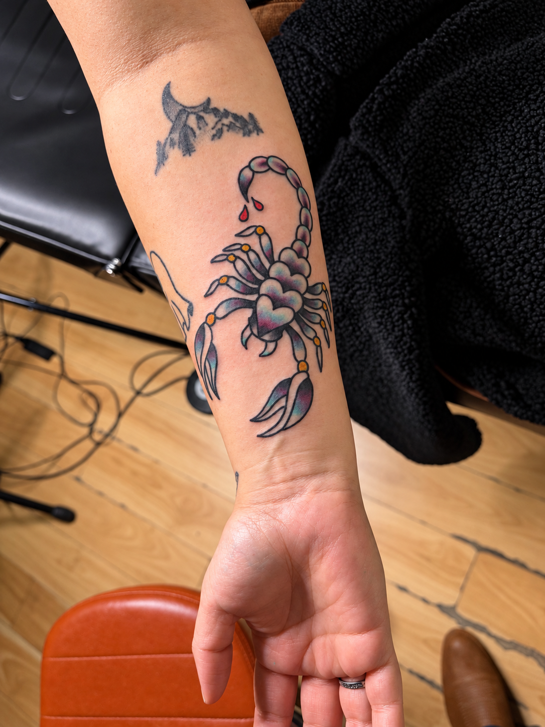 Colorful scorpion tattoo with a heart-shaped body and red teardrops on a forearm, work by Ruben.