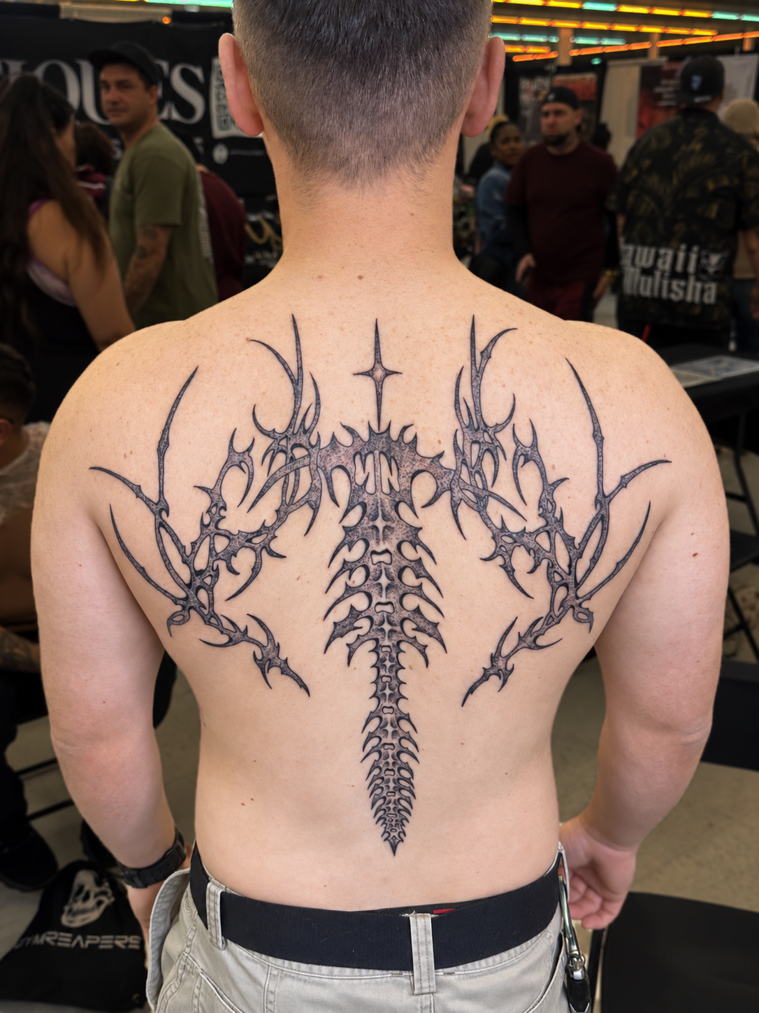 Large black-and-gray cyber tattoo spanning a man's upper back at a tattoo convention, work by Hannah.