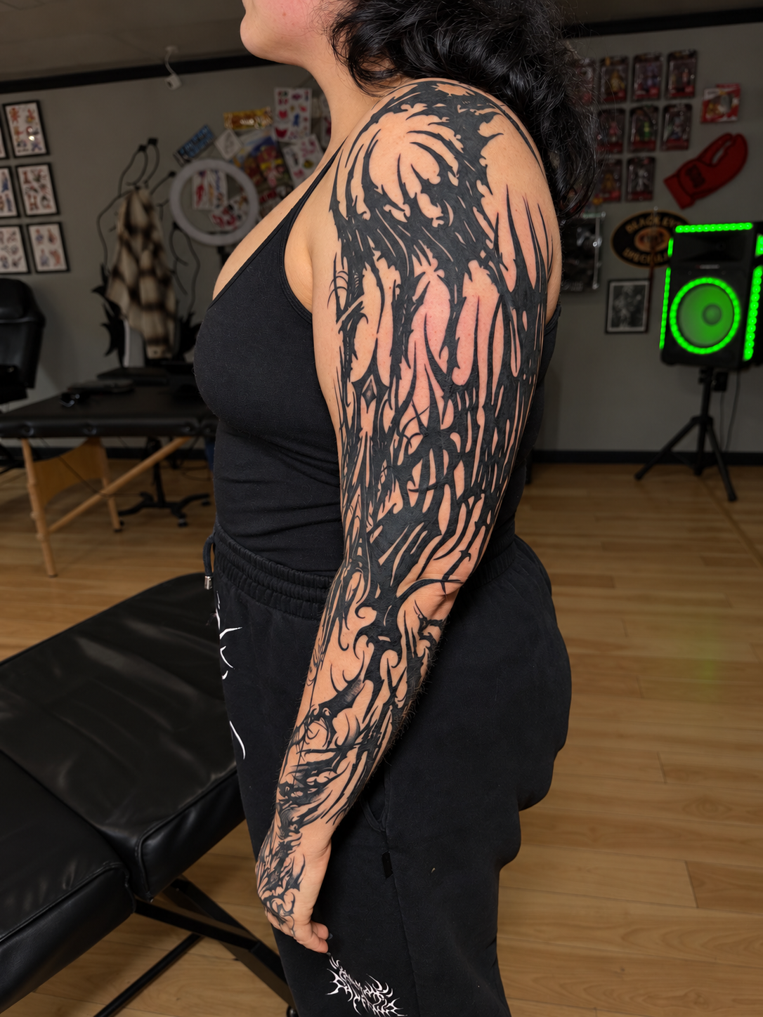 Person showcasing a large black-and-gray abstract tattoo covering the shoulder and full arm in a tattoo studio, work by Hannah.