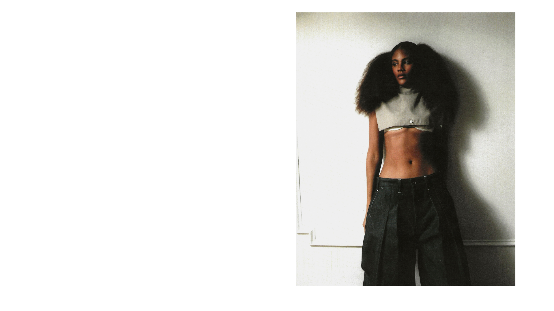 Fashion model with voluminous curly hair wearing a cropped gray top and black wide-leg pants