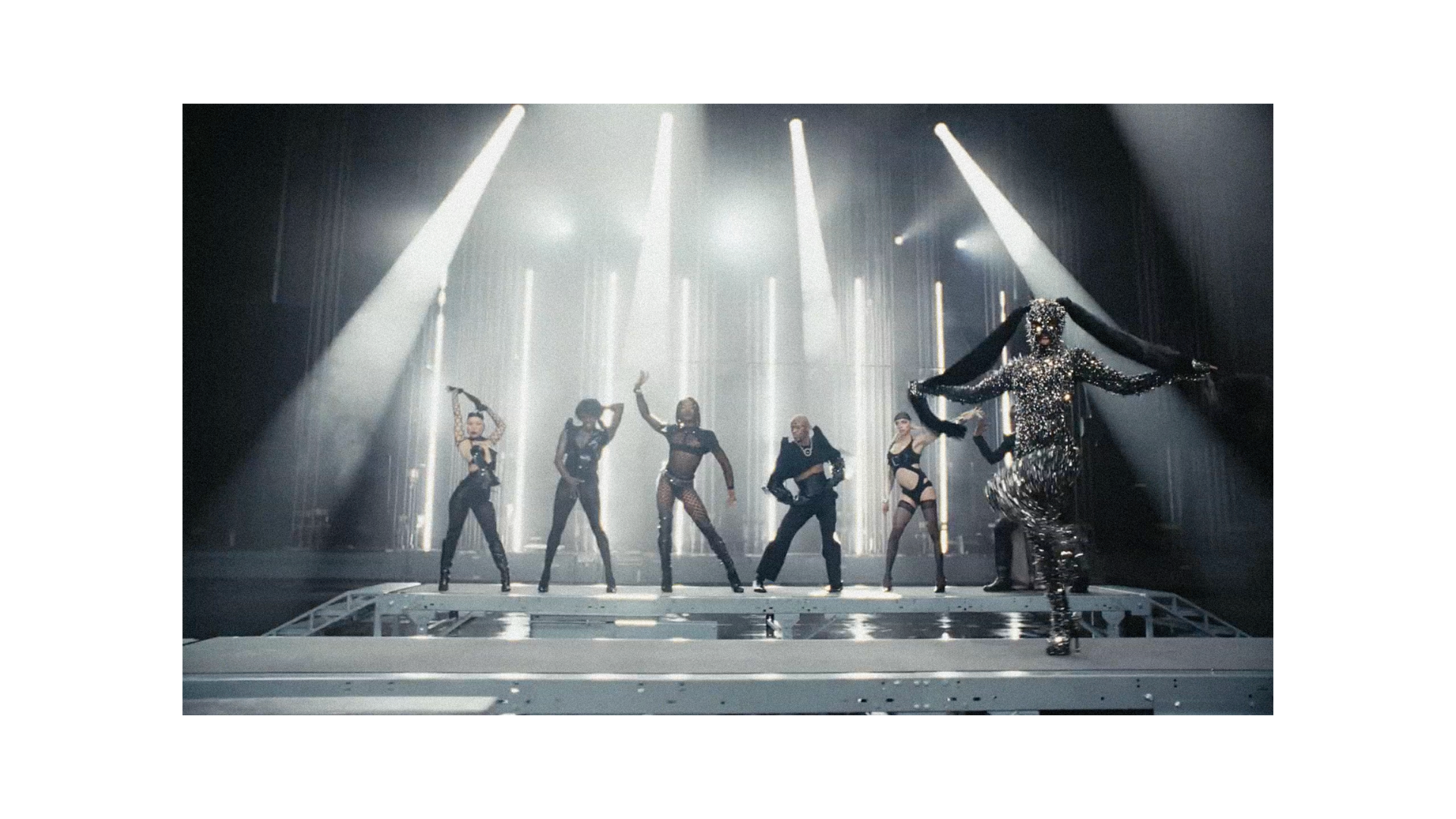Futuristic stage performance featuring a performer in a reflective silver costume and backup dancers under dramatic spotlights