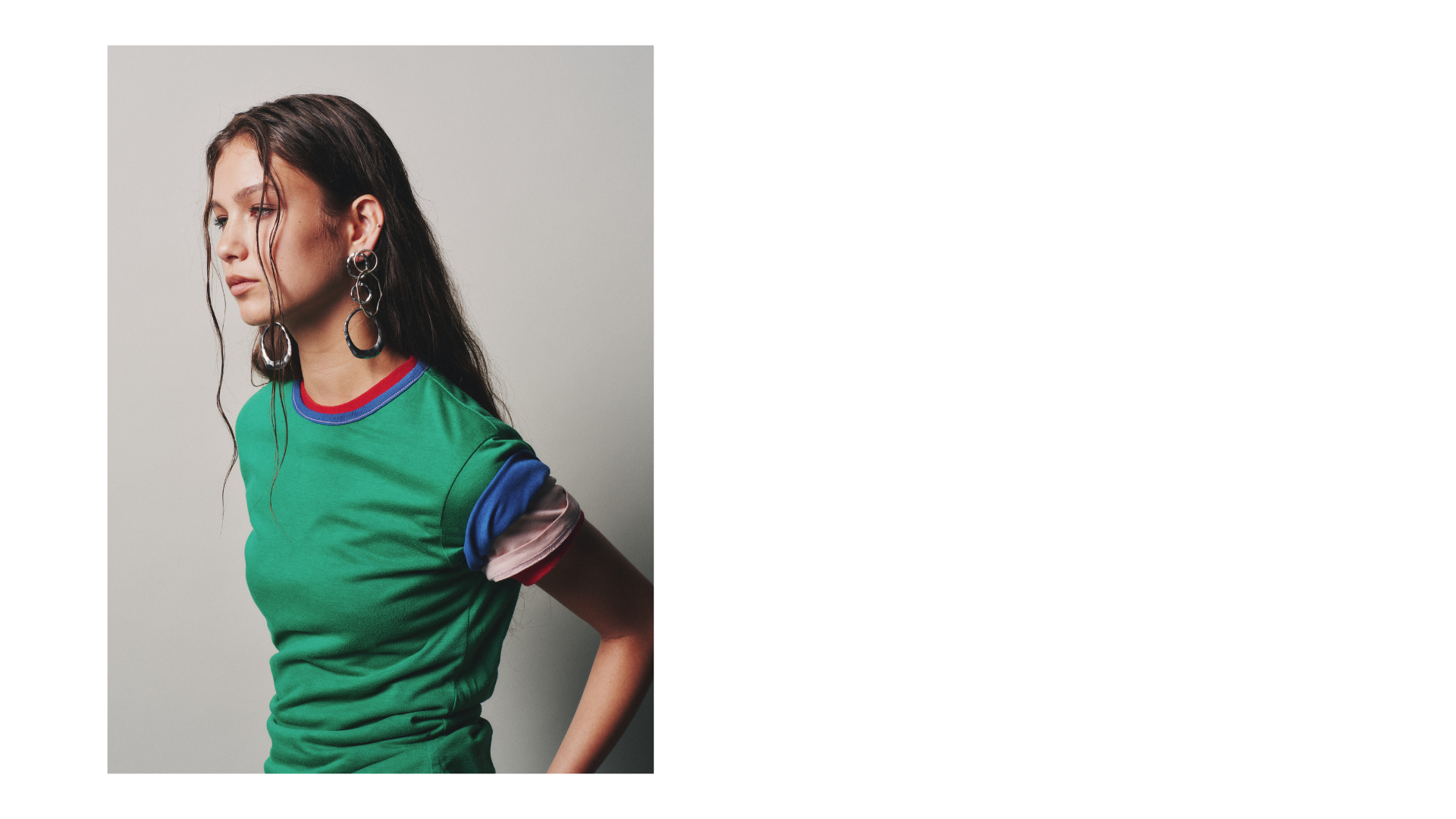 Woman with long dark hair wearing large hoop earrings and a green shirt with colorful striped sleeves