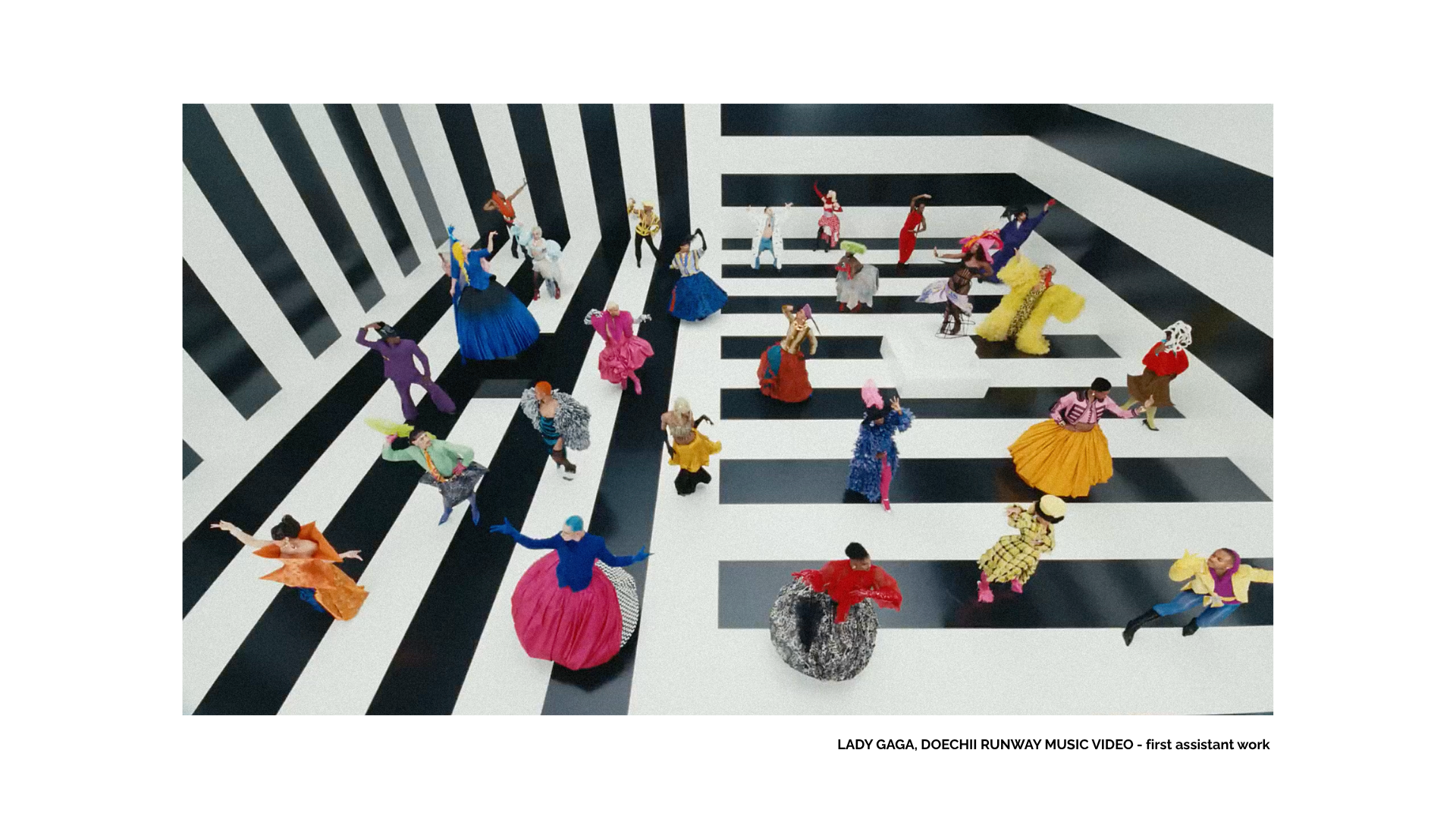 Aerial view of diverse dancers in colorful costumes performing on a giant black-and-white geometric piano-key floor.