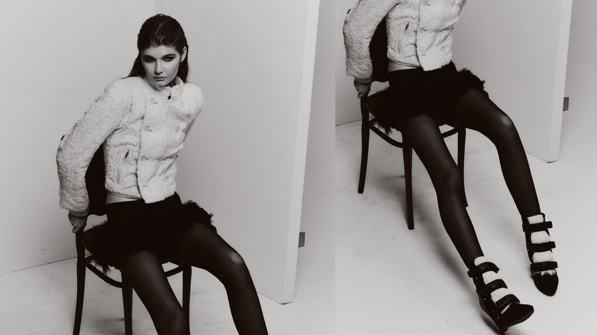 Black-and-white fashion editorial showing a model in a textured white jacket, black skirt, tights, and strappy heels seated on a chair.