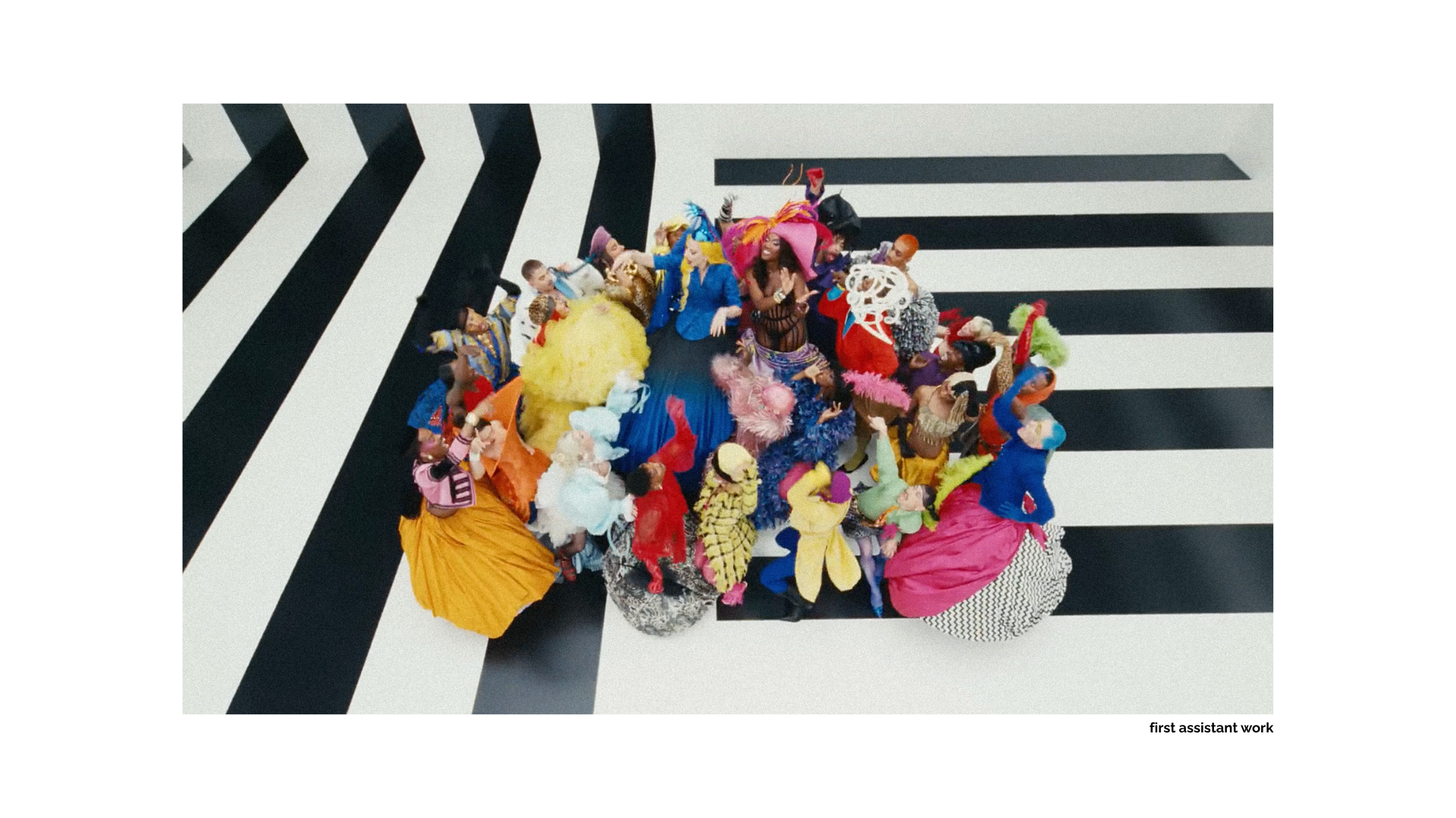 Large group of performers in colorful costumes posing on a black-and-white geometric stage