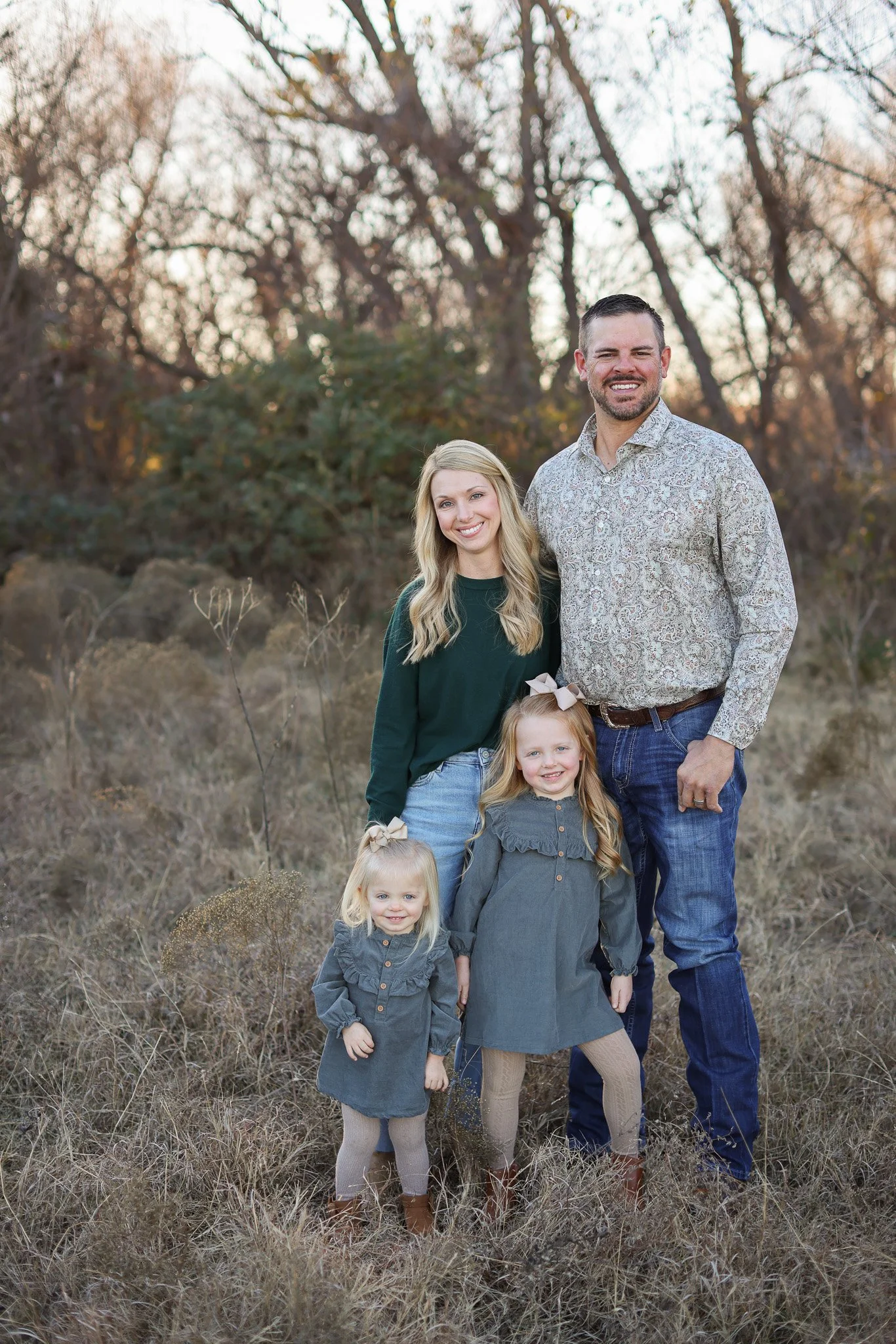 Family of four posing outdoors in a grassy wooded area