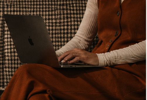 Person in a rust-colored vest using a laptop on their lap