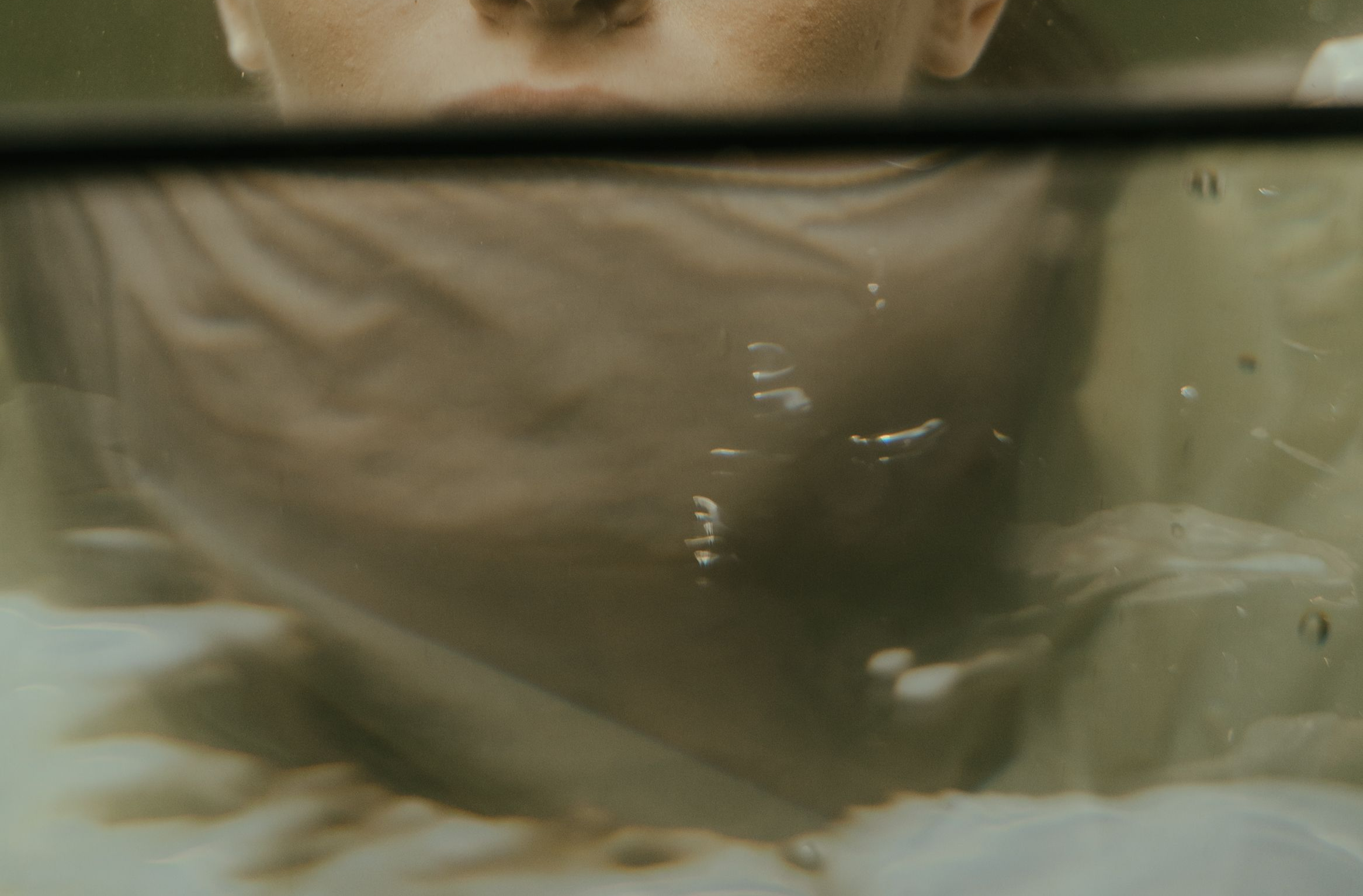 Abstract close-up of muted olive-green textures and soft reflections with a cinematic, editorial feel.