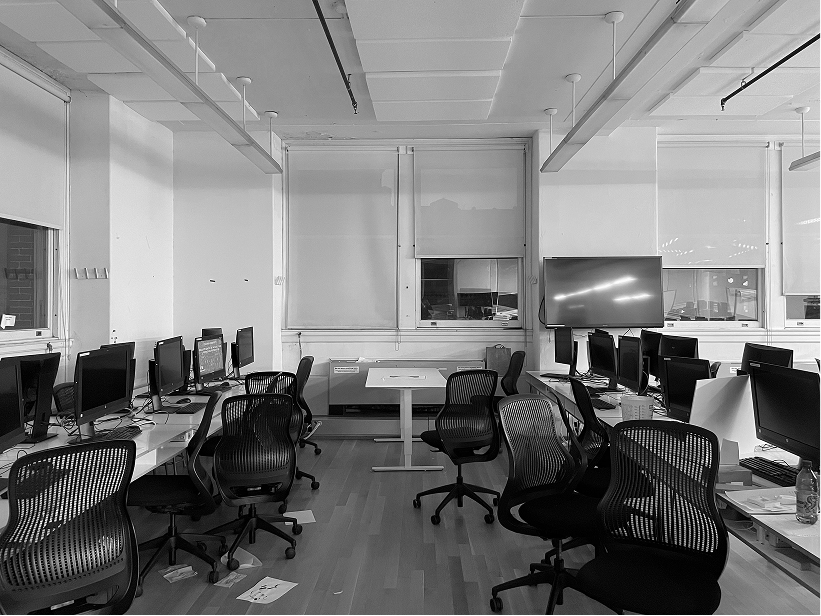 Empty computer lab with rows of desktop monitors, black office chairs, and wall-mounted screens