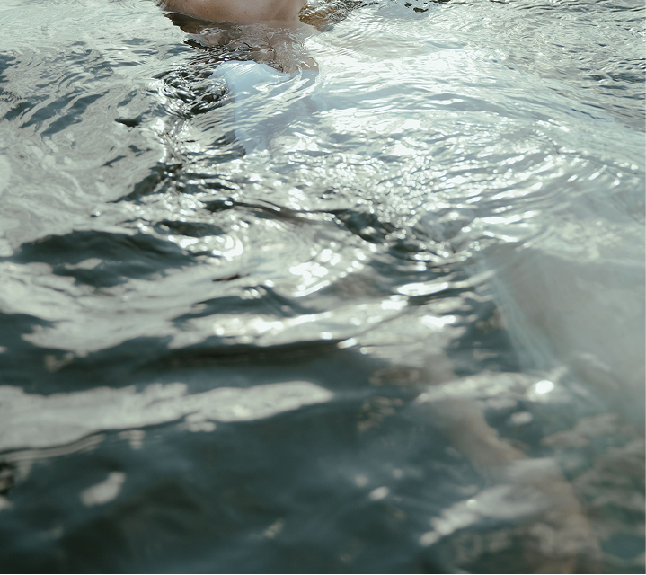 Close-up of sunlight reflecting on rippling blue-green water with a partially submerged swimmer