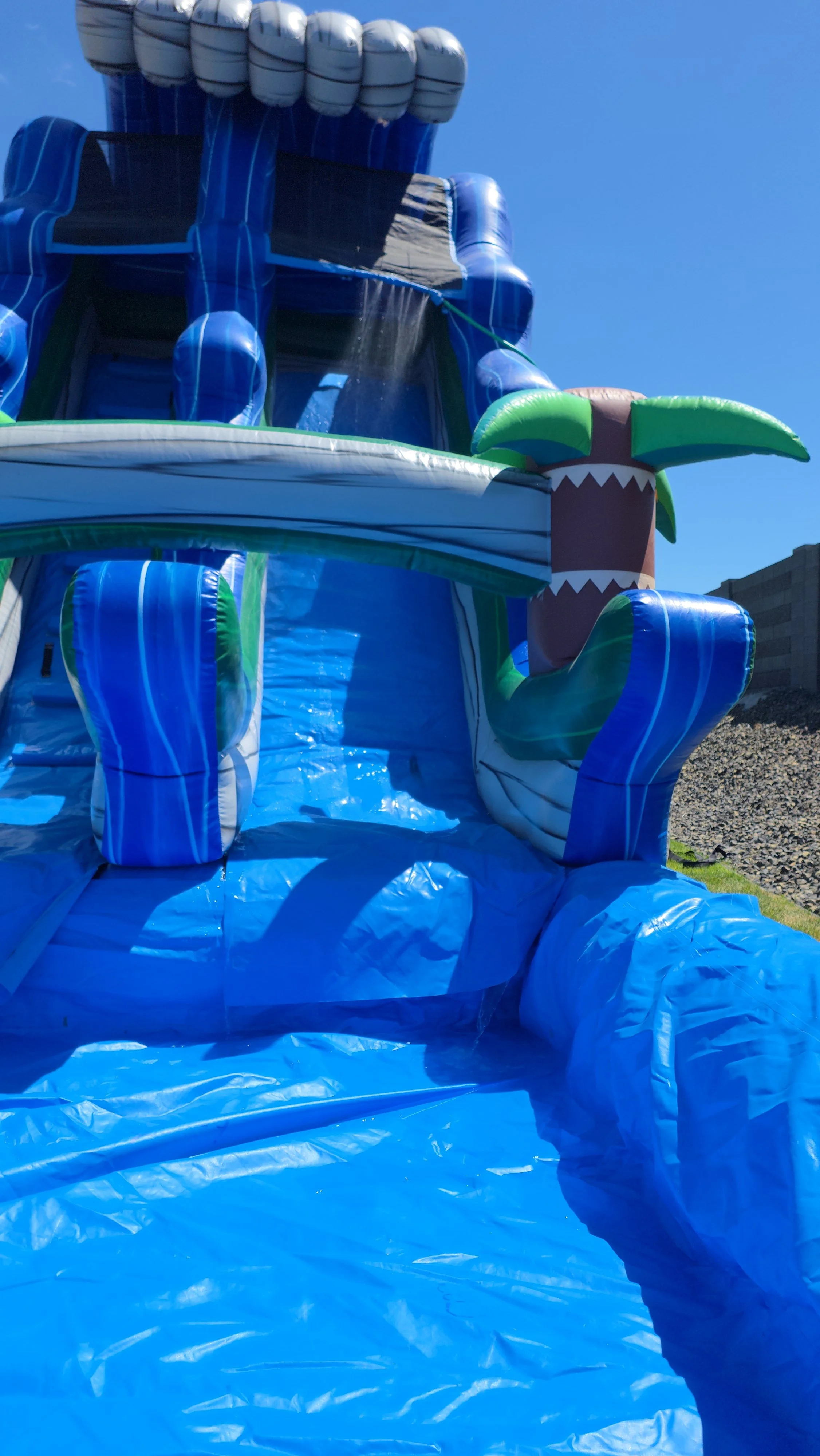 Side view of The Lu'au inflatable waterslide showing its tropical design, tall slide structure and backyard setup.