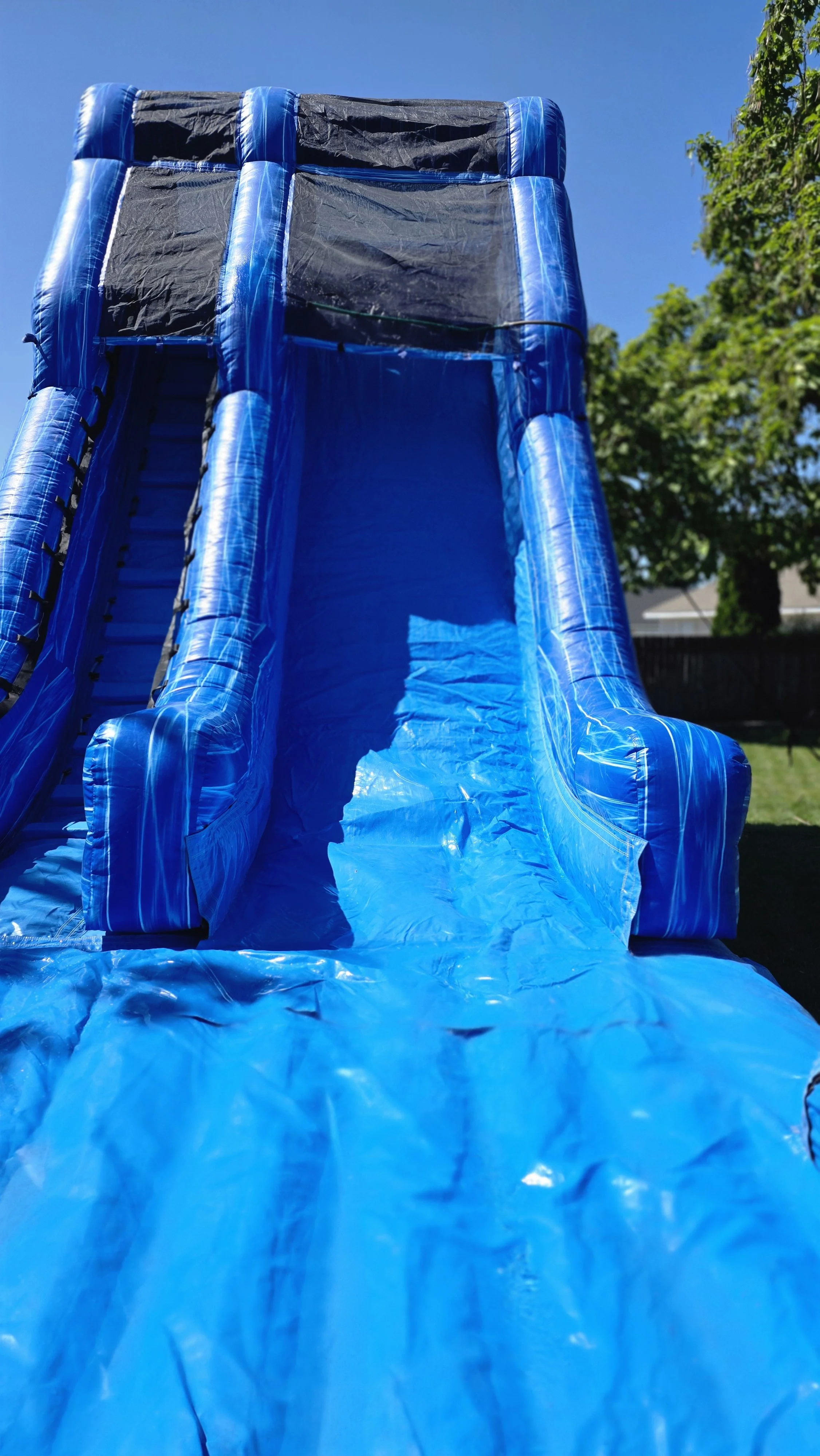 Close-up of Big Blue's towering inflatable waterslide with two blue sliding lanes and protective safety netting, available for backyard parties in the Tri-Cities, Washington.