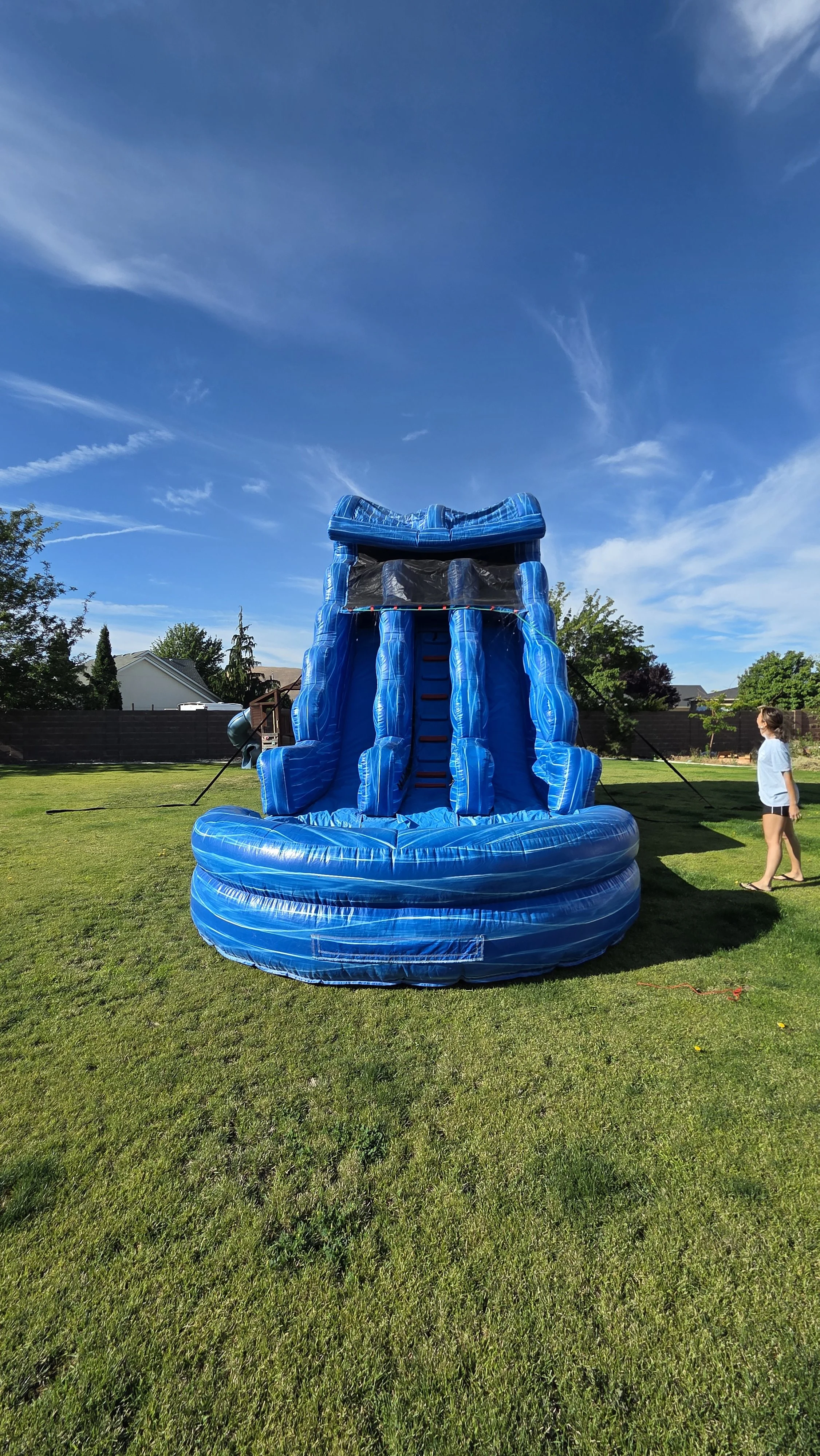 Front view of the towering Double Trouble blue inflatable waterslide with two racing lanes, set up on a sunny backyard lawn.