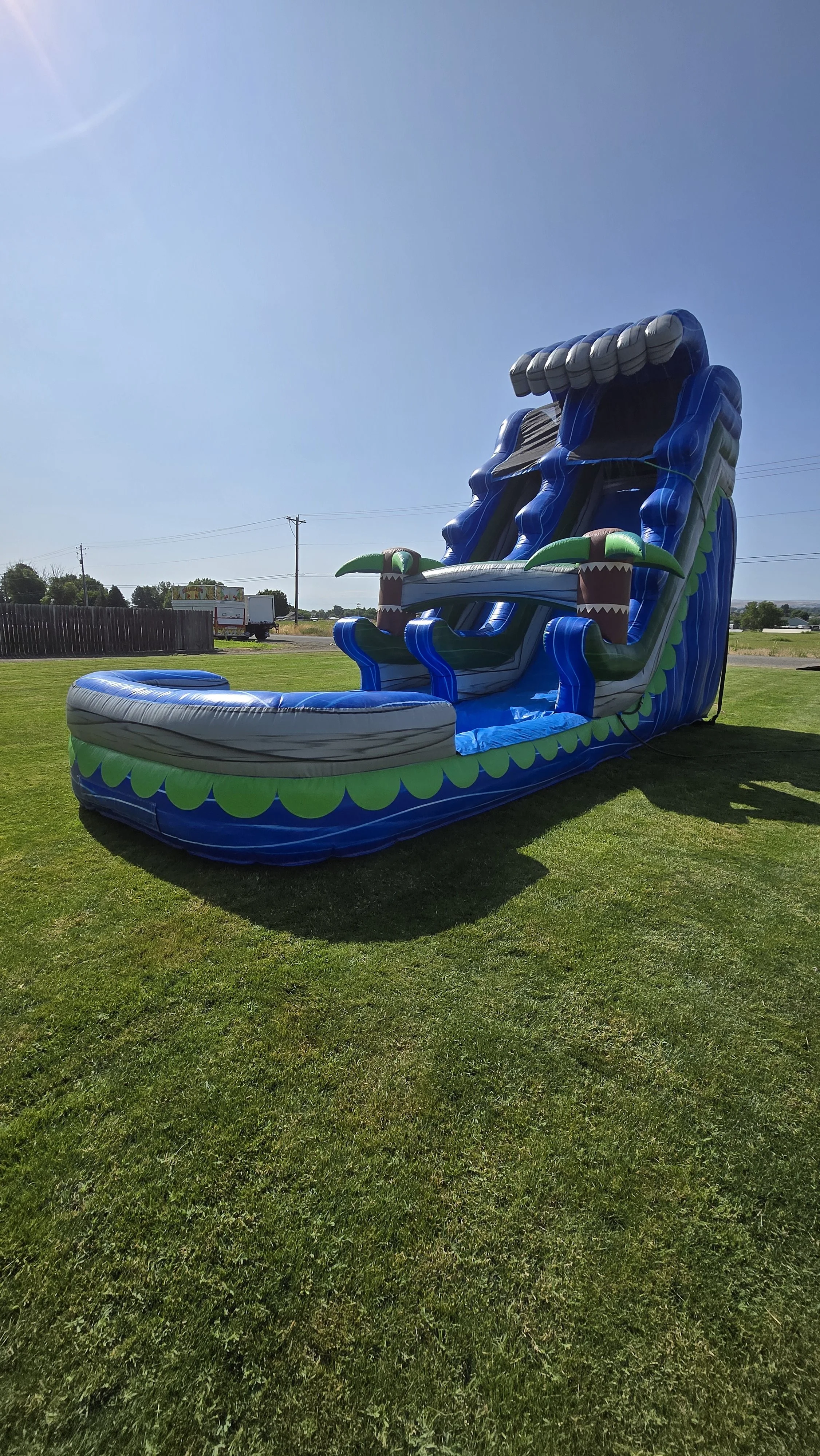 Front view of The Lu'au tropical inflatable waterslide with bright blue and green colors, palm-tree decorations and a large splash pool.
