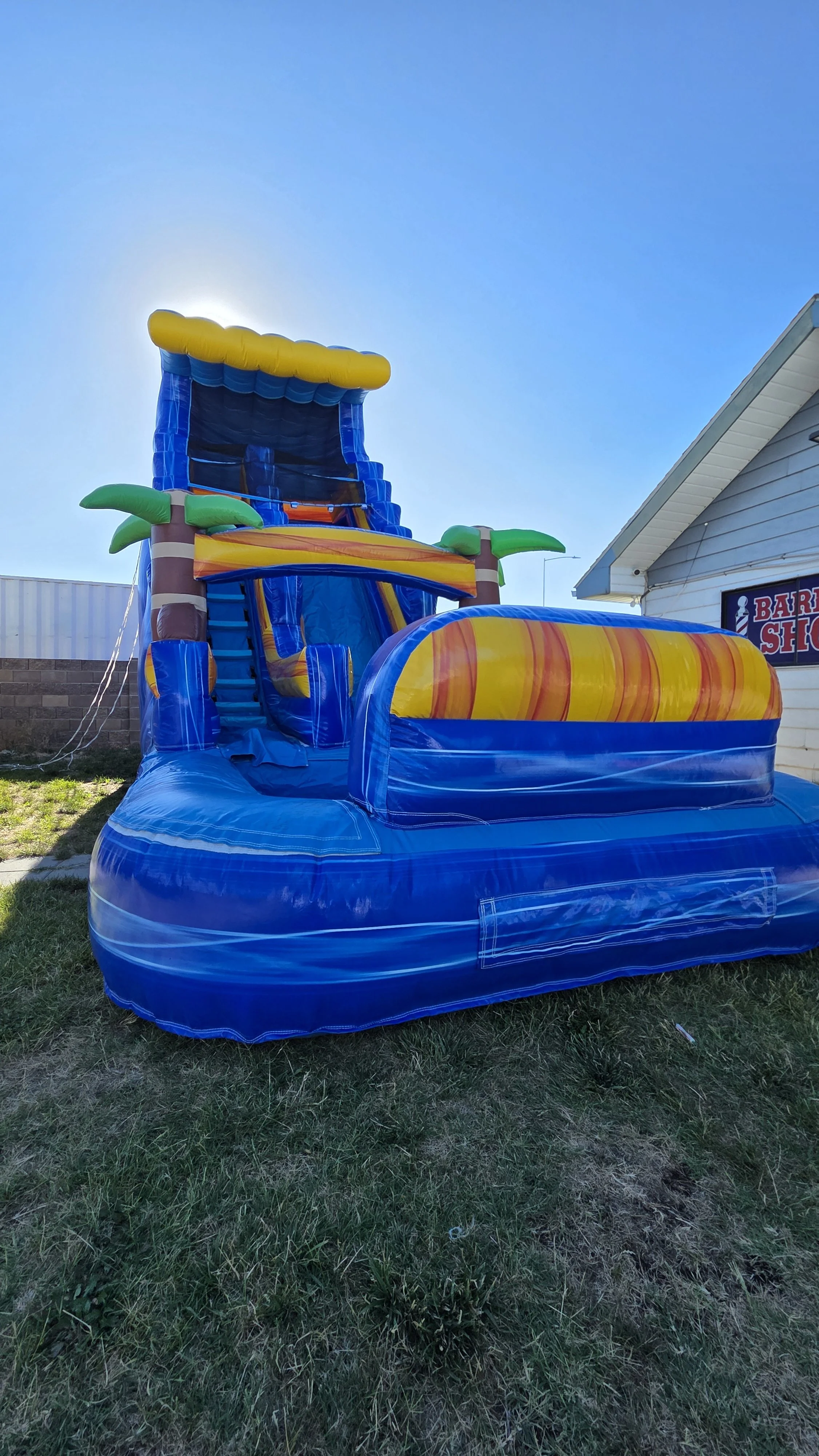 Side view of the Crazy Coconut tropical inflatable waterslide with palm-tree decorations, set up outdoors on a sunny day.