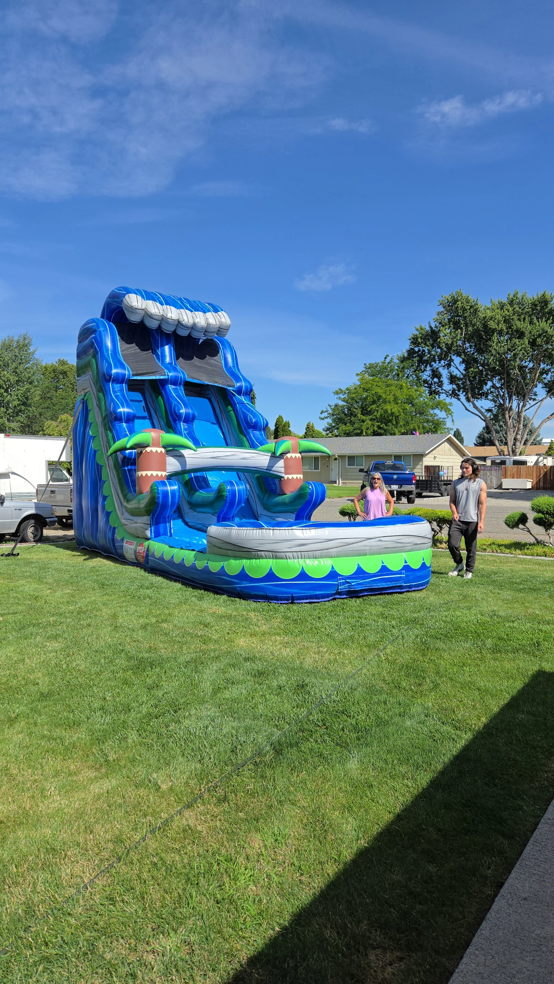 Side view of The Lu'au inflatable waterslide showing its tropical design, tall slide structure and backyard setup.