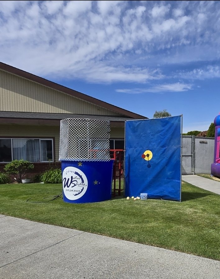 Dunk Dynasty blue dunk tank rental set up outdoors with target wall, safety netting and throwing area for a carnival-style event.