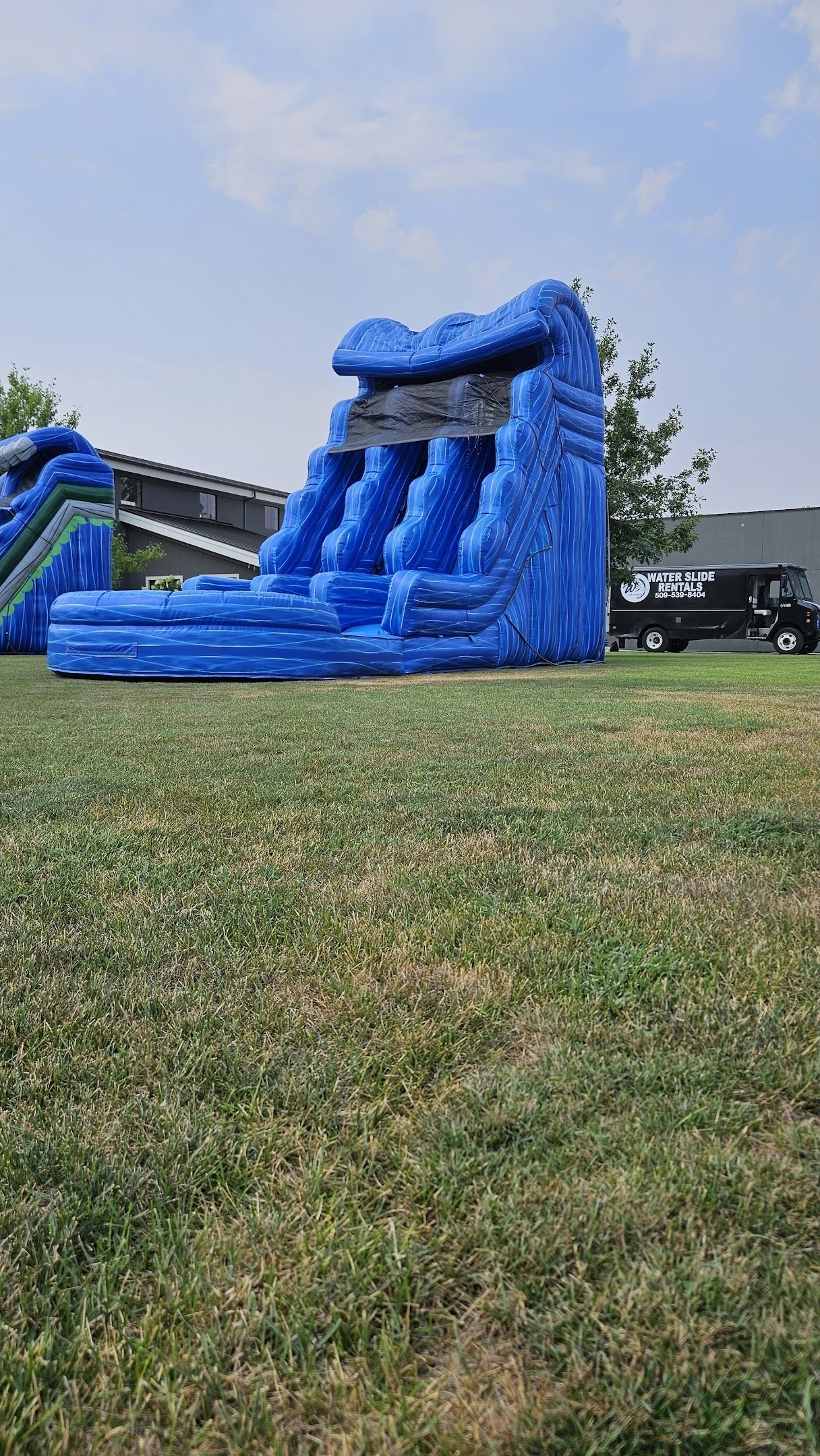 Double Trouble 30-foot-tall blue inflatable waterslide set up on a grassy lawn beside a Waterslides Kennewick delivery truck in the Tri-Cities, Washington.