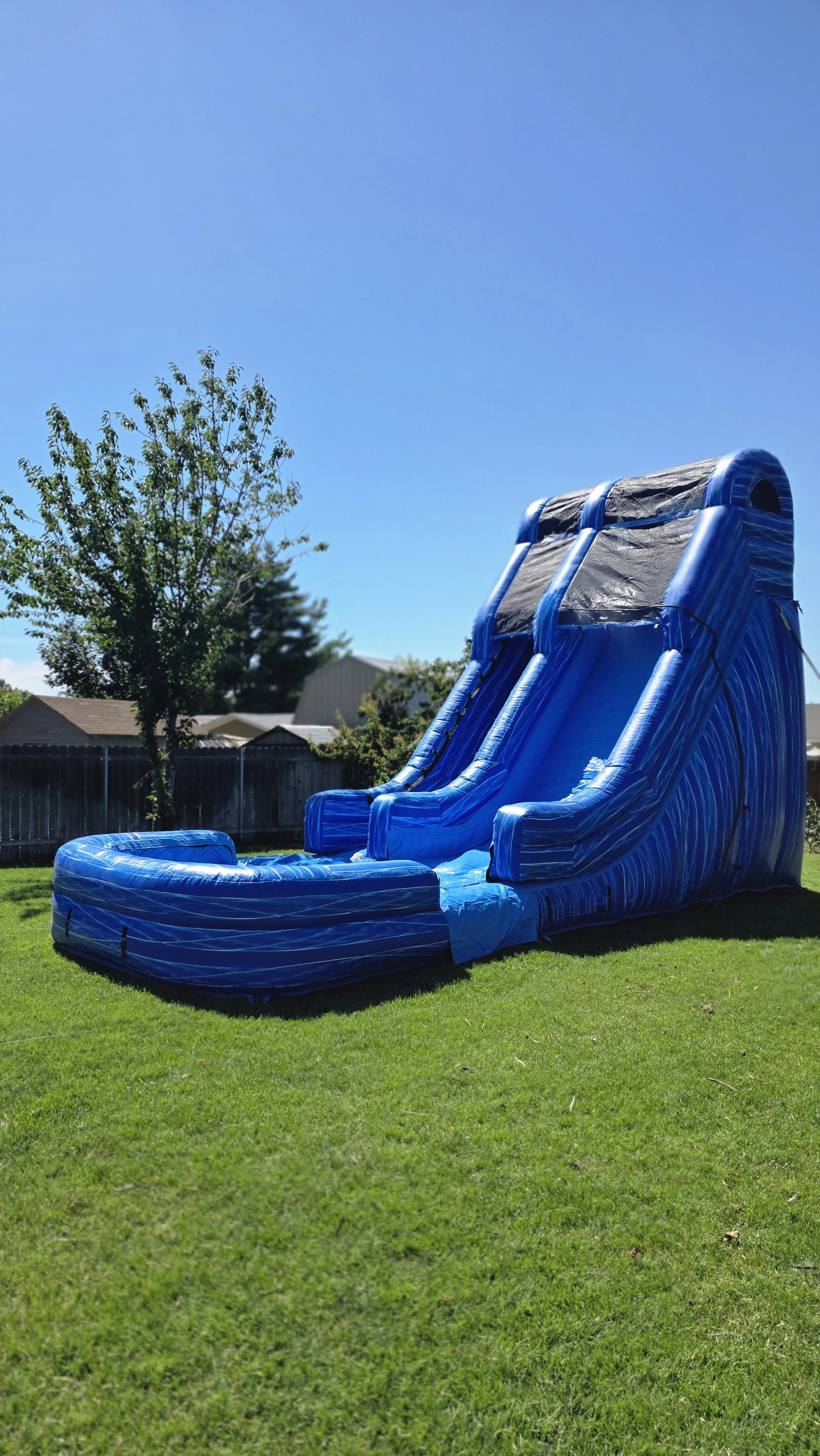 Side view of the towering Big Blue inflatable waterslide set up on a sunny backyard lawn for a summer party in the Tri-Cities, WA.