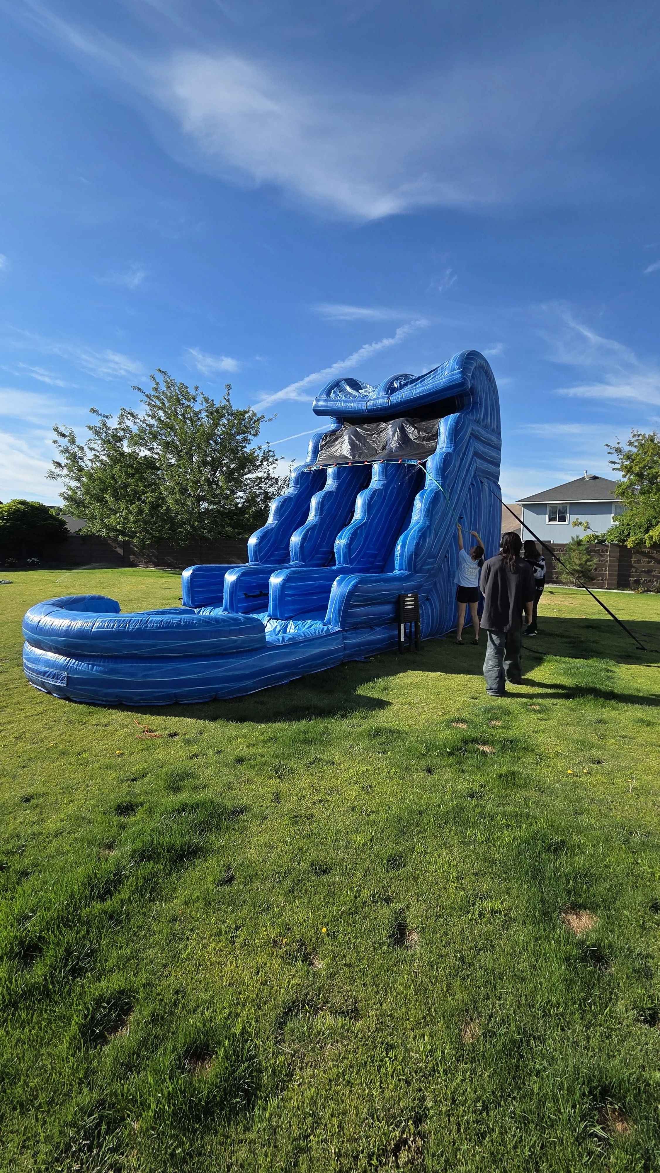 Double Trouble 30-foot inflatable waterslide standing on a spacious grassy lawn with people nearby, showing the scale of this large party rental.