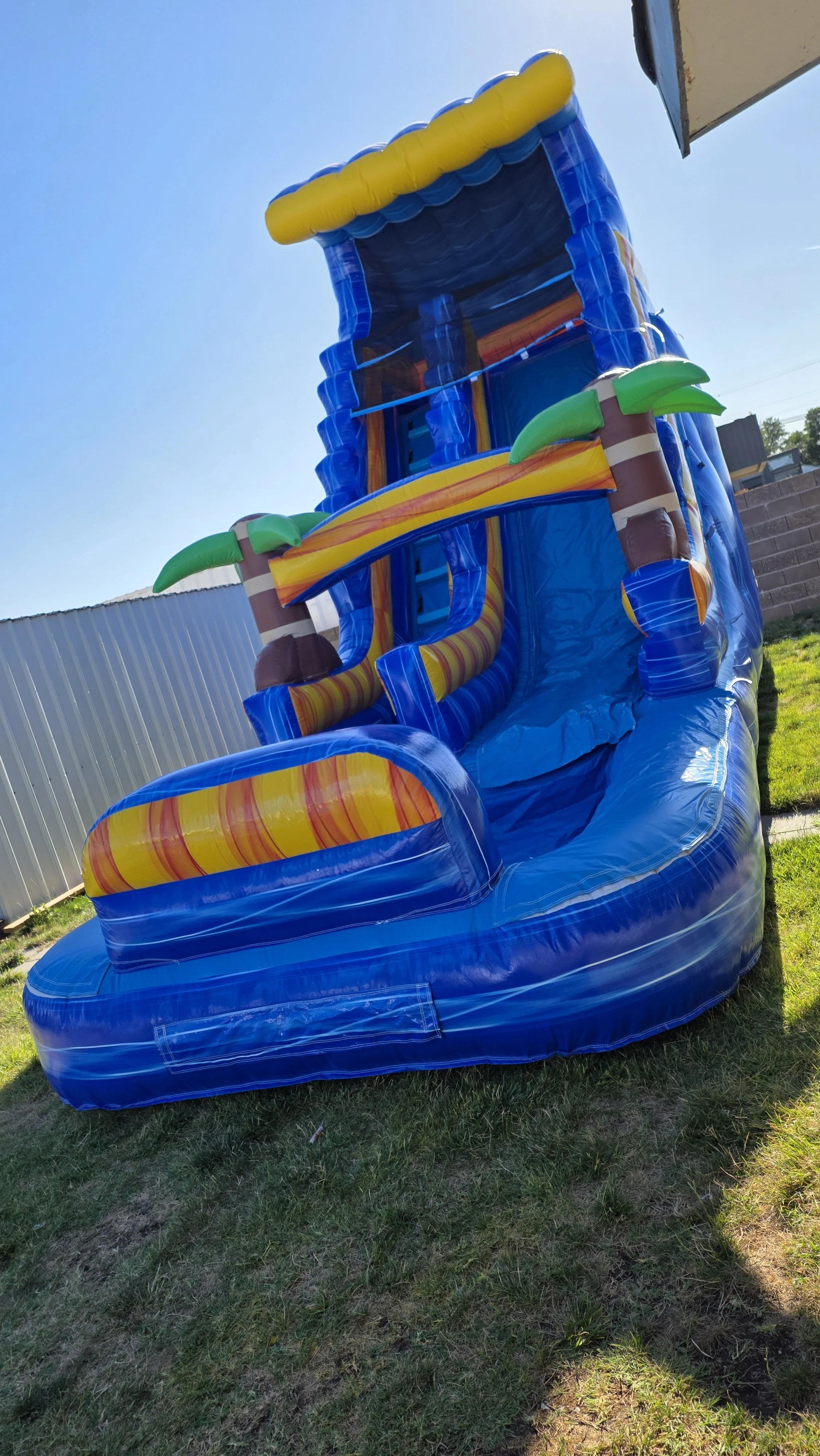Side view of the Crazy Coconut tropical inflatable waterslide with palm-tree decorations, set up outdoors on a sunny day.