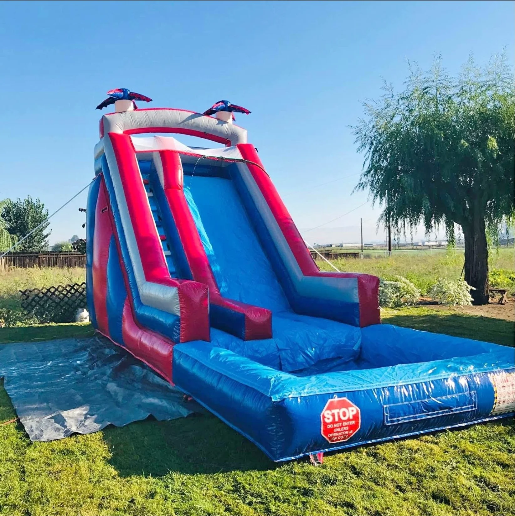 Red, blue, and white inflatable water slide with a splash pool set up on a grassy lawn.