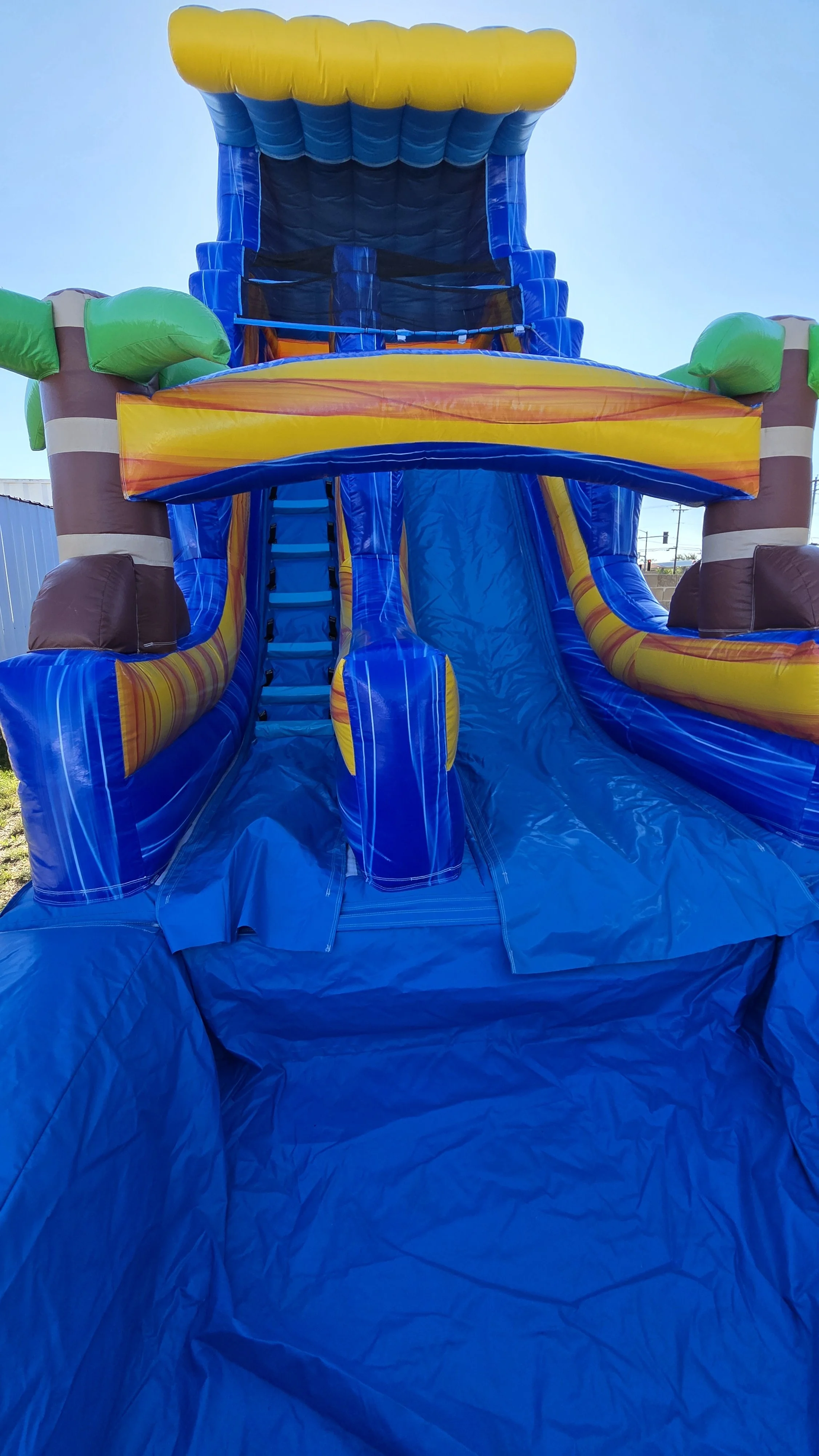 Front view of the Crazy Coconut tropical inflatable waterslide showing its blue climbing section and colorful upper structure for backyard parties.