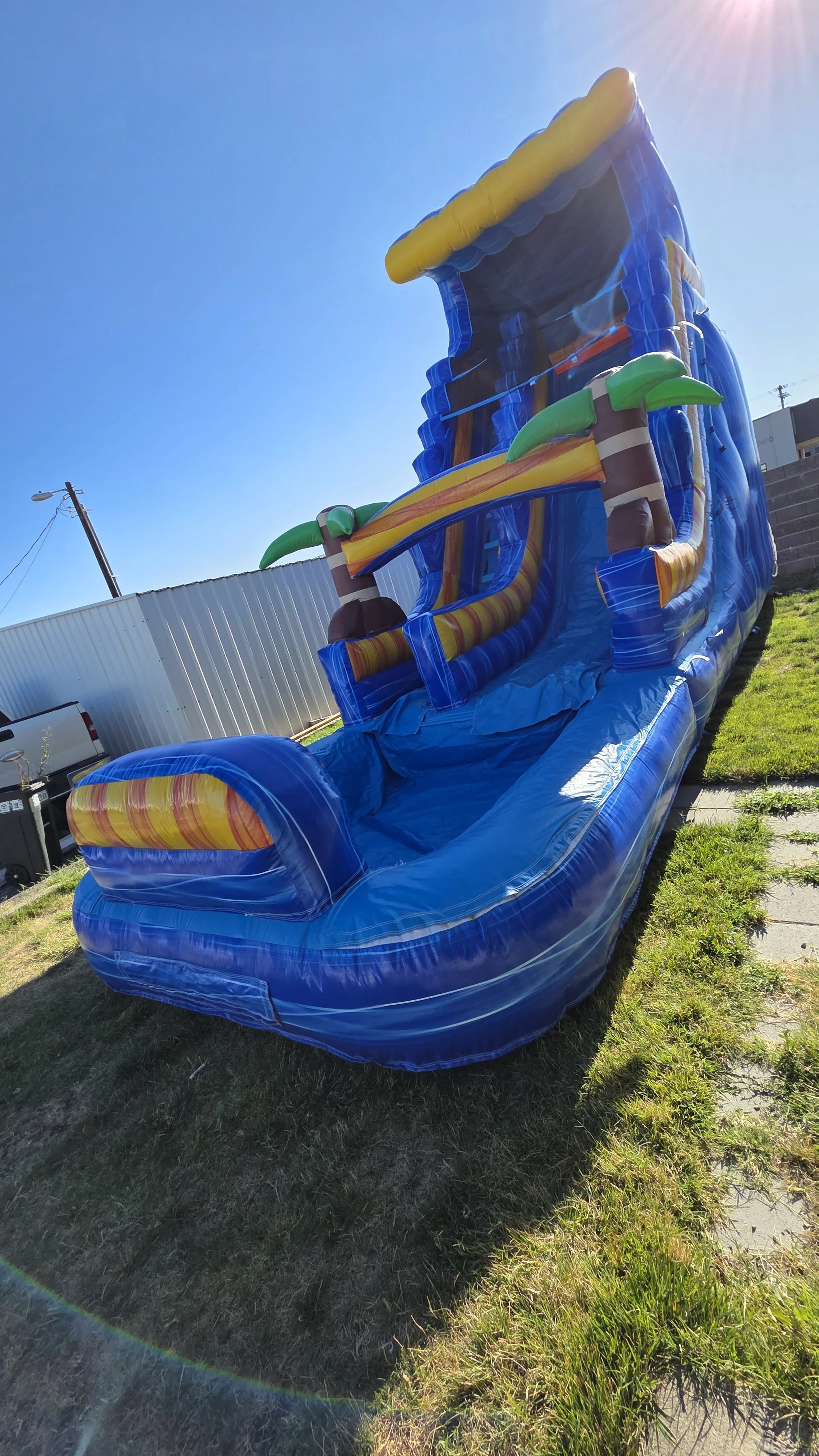 Side view of the Crazy Coconut tropical inflatable waterslide with palm-tree decorations, set up outdoors on a sunny day.