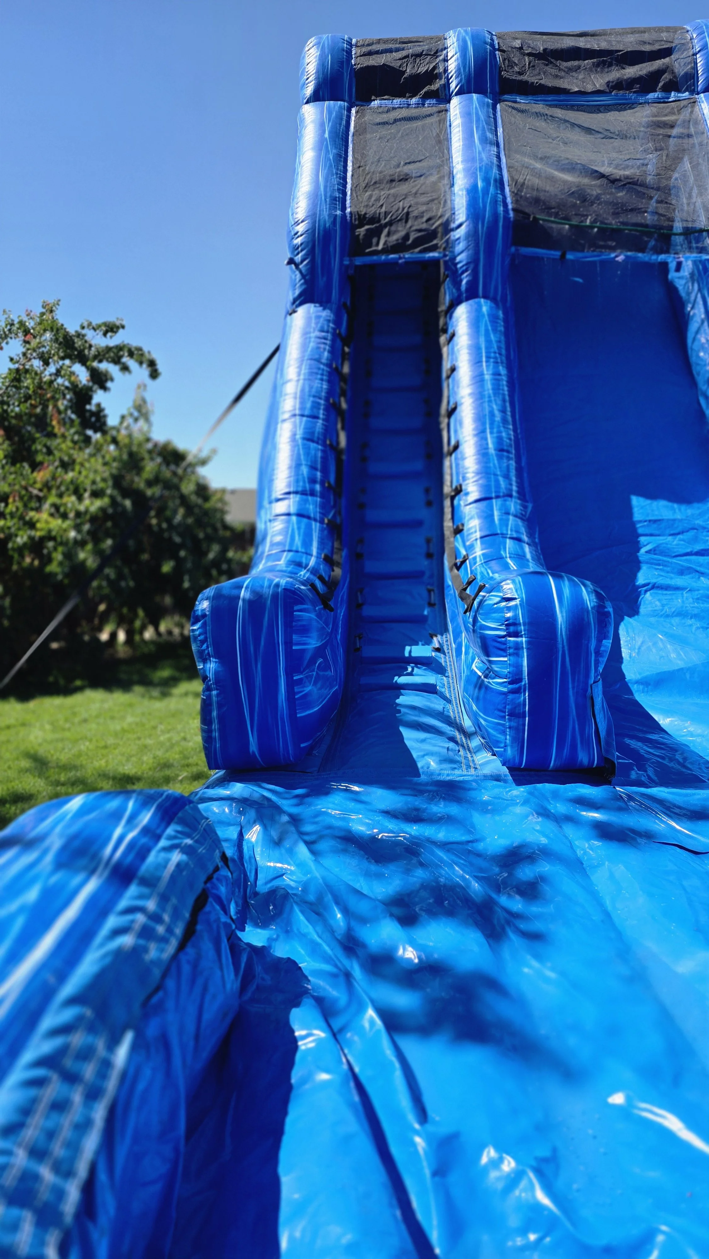 Close-up of Big Blue's blue inflatable waterslide lanes and climbing ladder, available for backyard party rentals in Richland, Washington.
