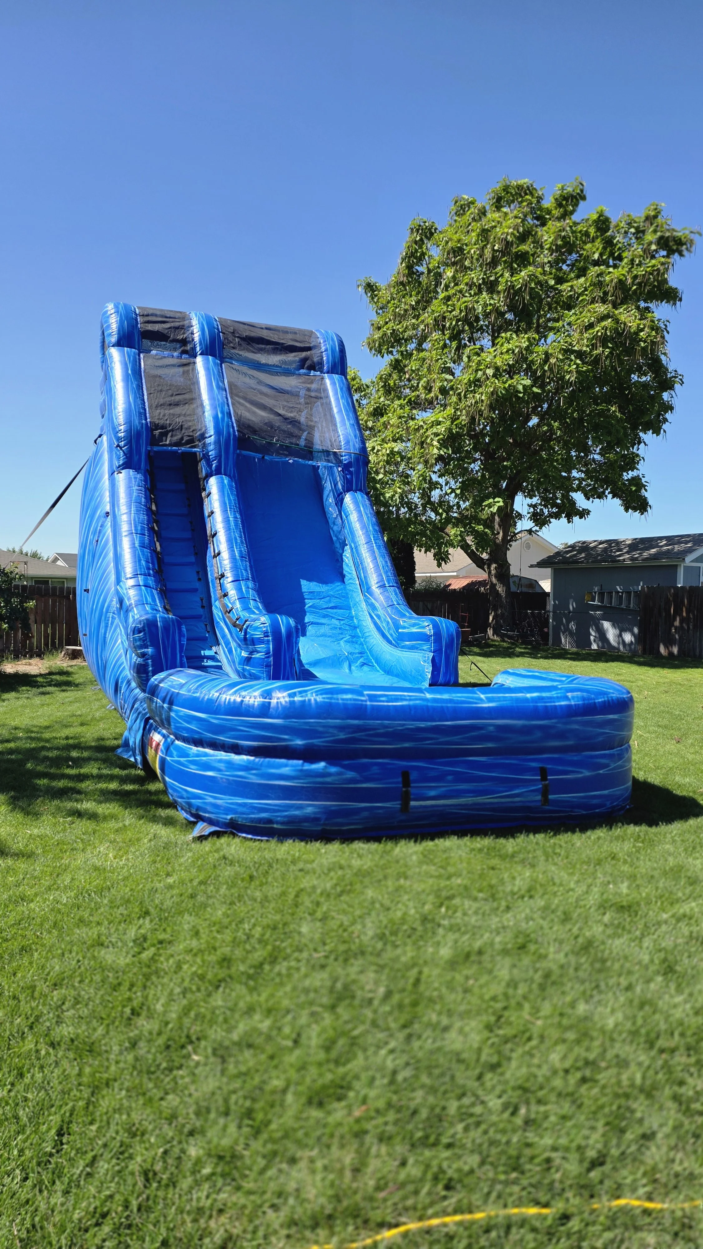 Big Blue inflatable waterslide standing on a grassy backyard lawn, showing its large size for outdoor celebrations in Kennewick, Pasco and Richland.