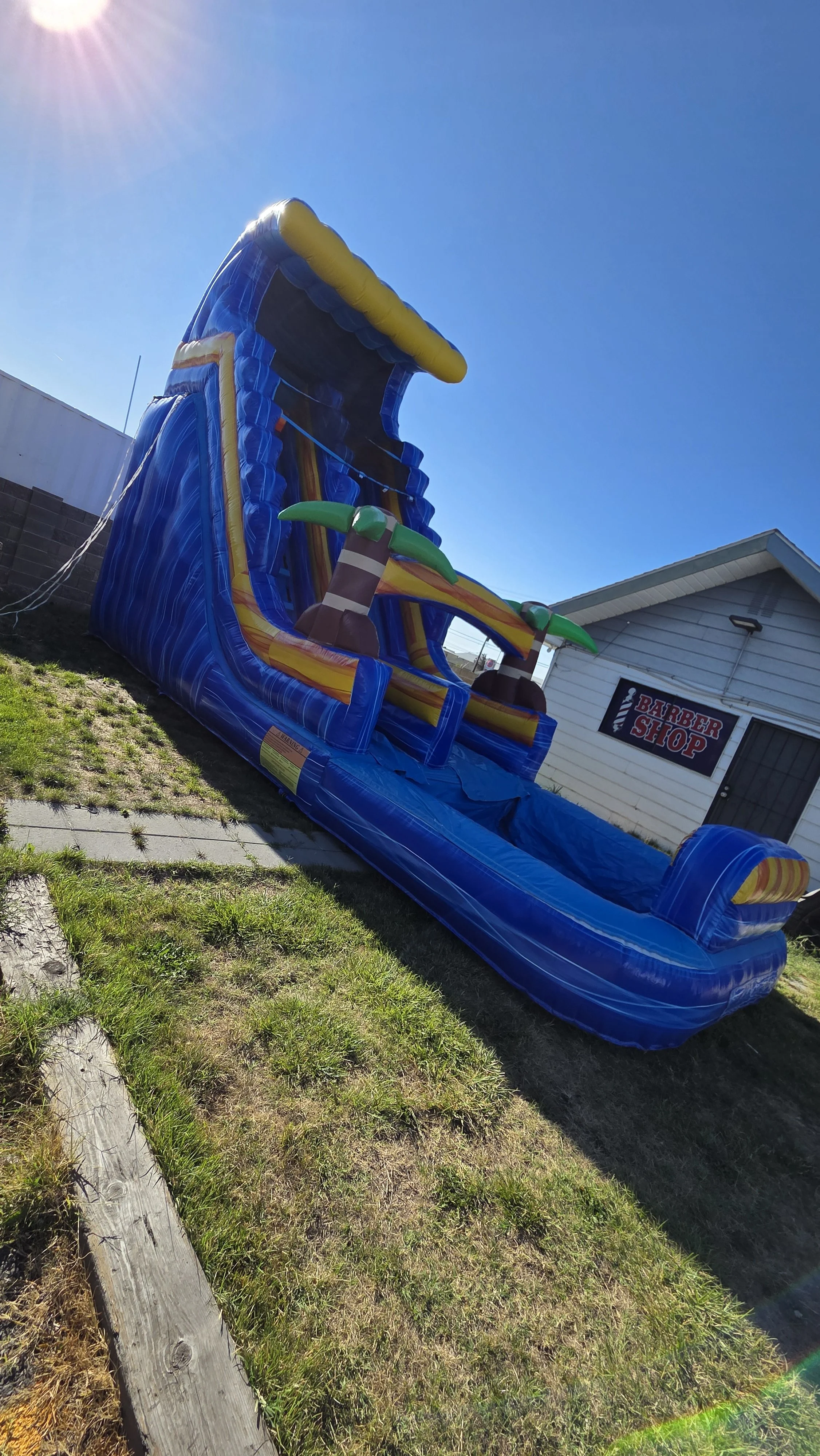 Side view of the Crazy Coconut tropical inflatable waterslide with palm-tree decorations, set up outdoors on a sunny day.