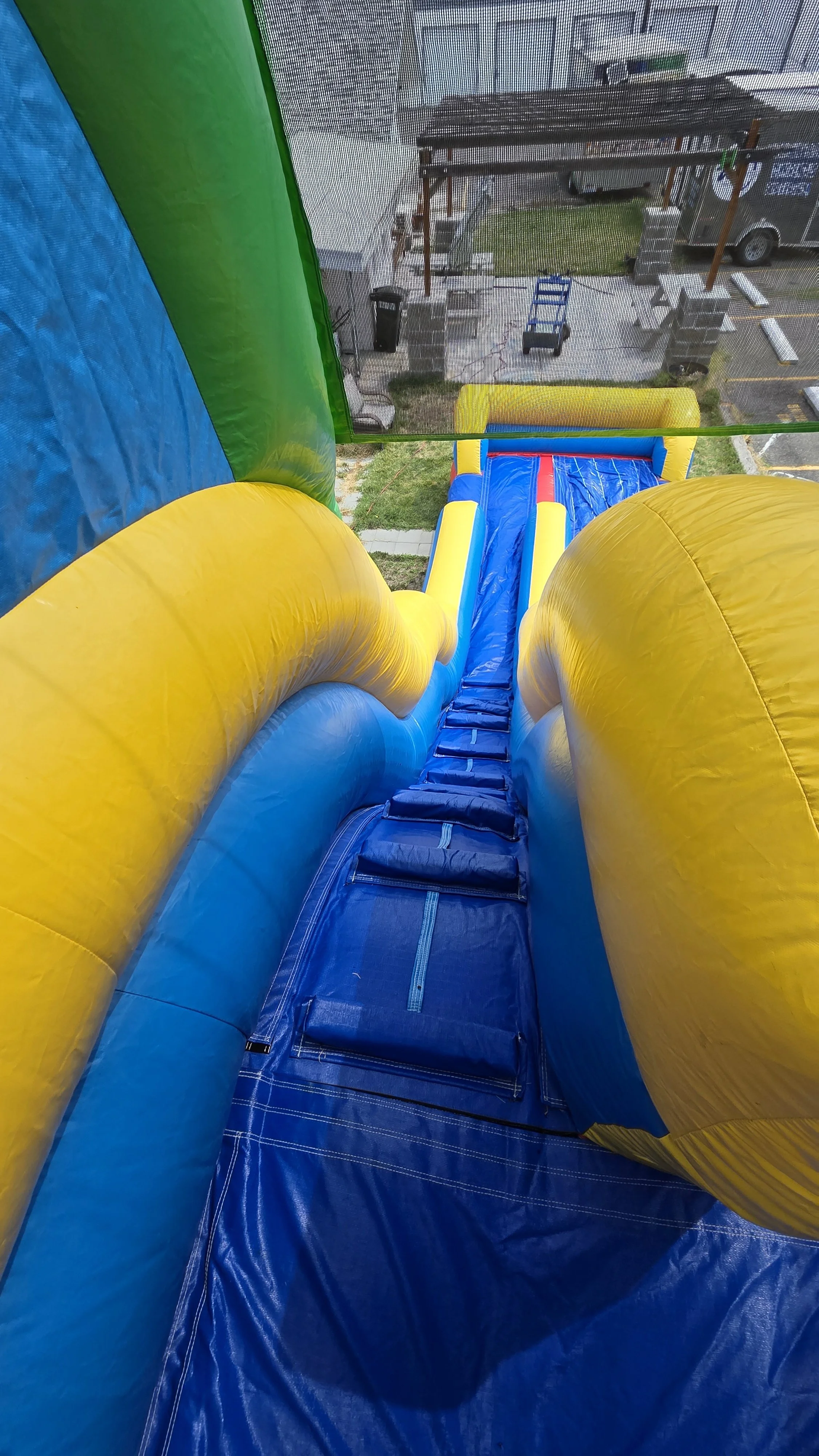 View from the top of the Flip Flop inflatable waterslide, looking down its blue sliding lane between bright yellow inflatable sides.