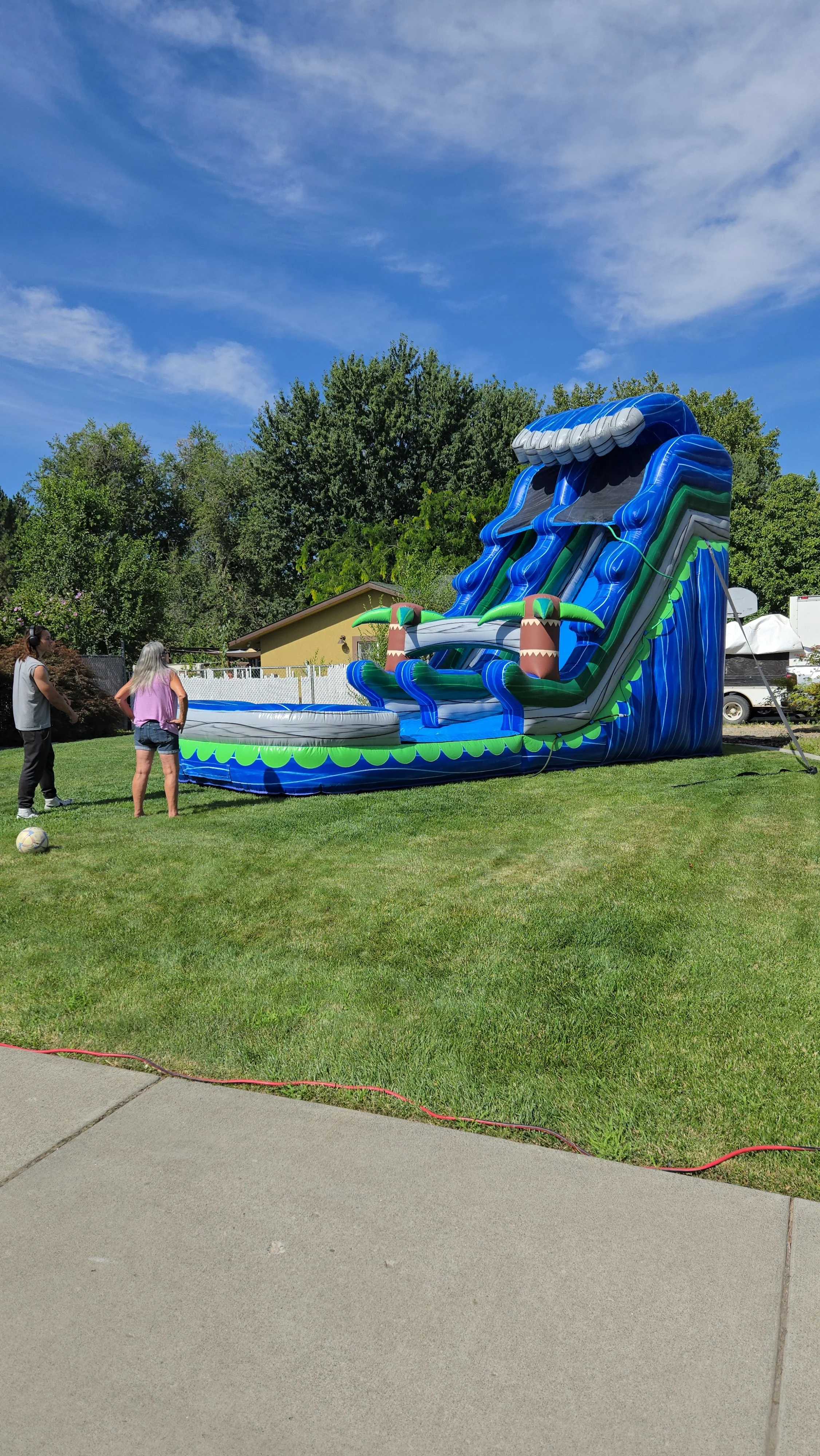 Side view of The Lu'au inflatable waterslide showing its tropical design, tall slide structure and backyard setup.