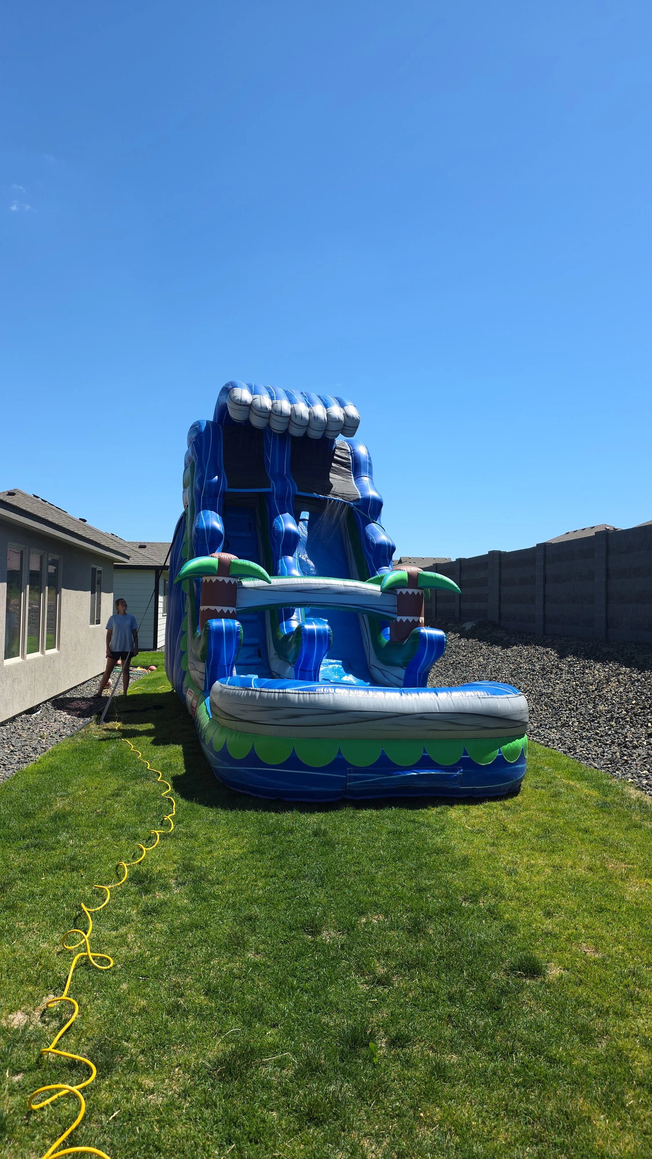Front view of The Lu'au tropical inflatable waterslide with bright blue and green colors, palm-tree decorations and a large splash pool.