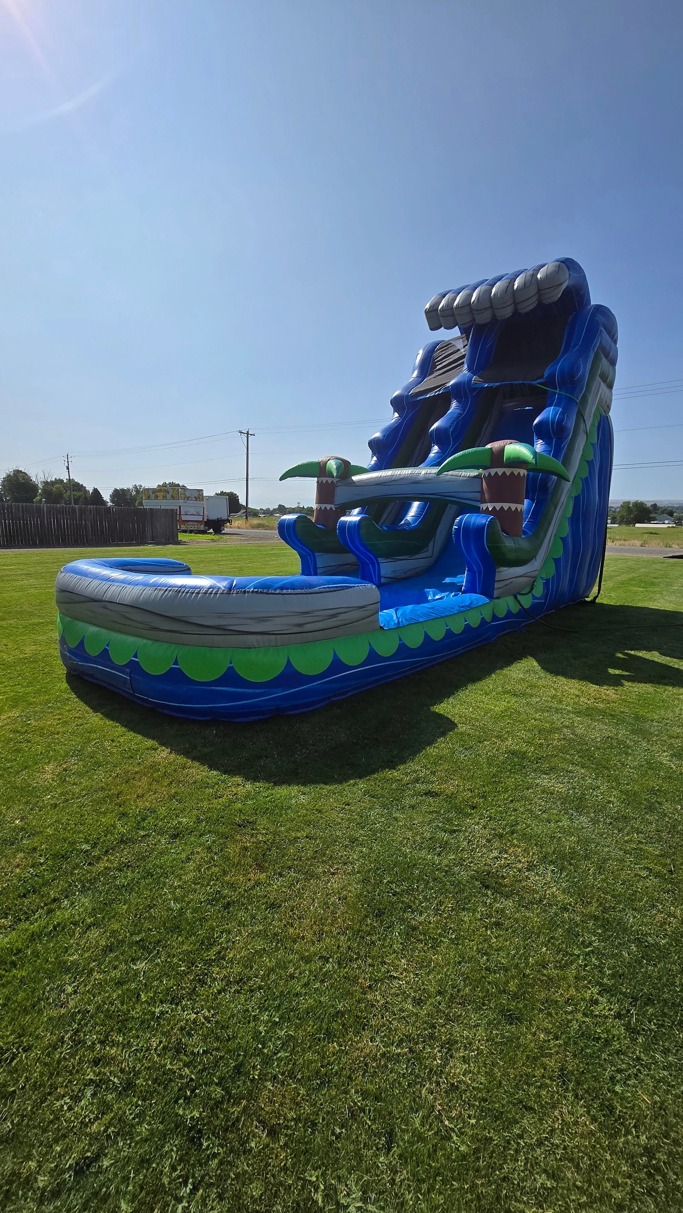 Front view of The Lu'au tropical inflatable waterslide with bright blue and green colors, palm-tree decorations and a large splash pool.